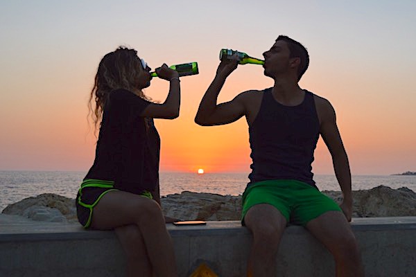 Man and a woman relaxing on a beach at sunset having a drink