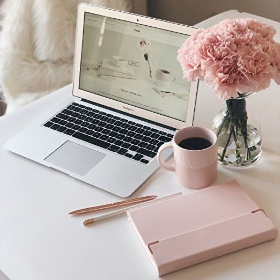 a laptop, journal, cup of coffee, and vase of flowers on a desk