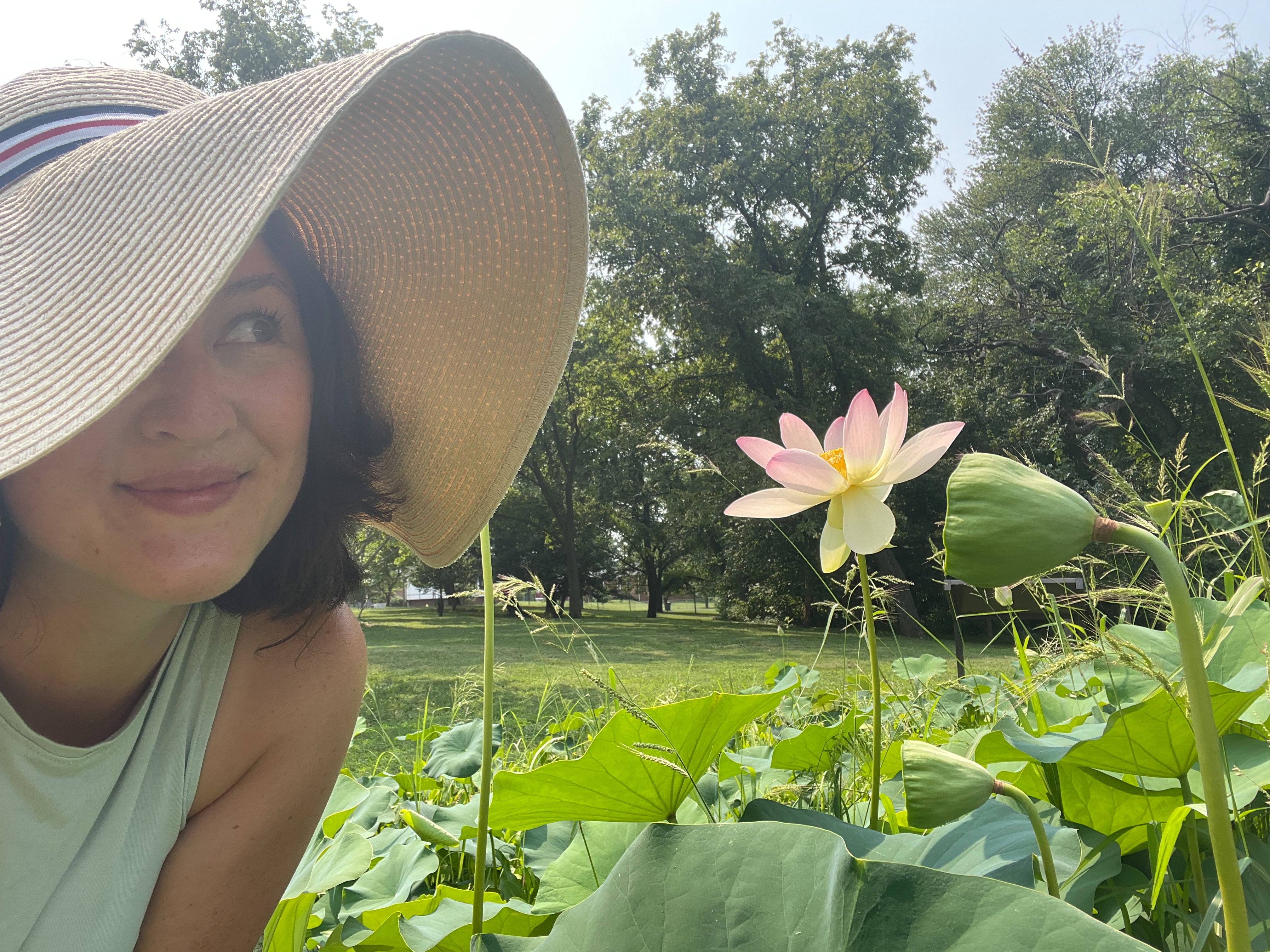 Su Kyong wearing a sun hat, amid trees and a lotus blossom