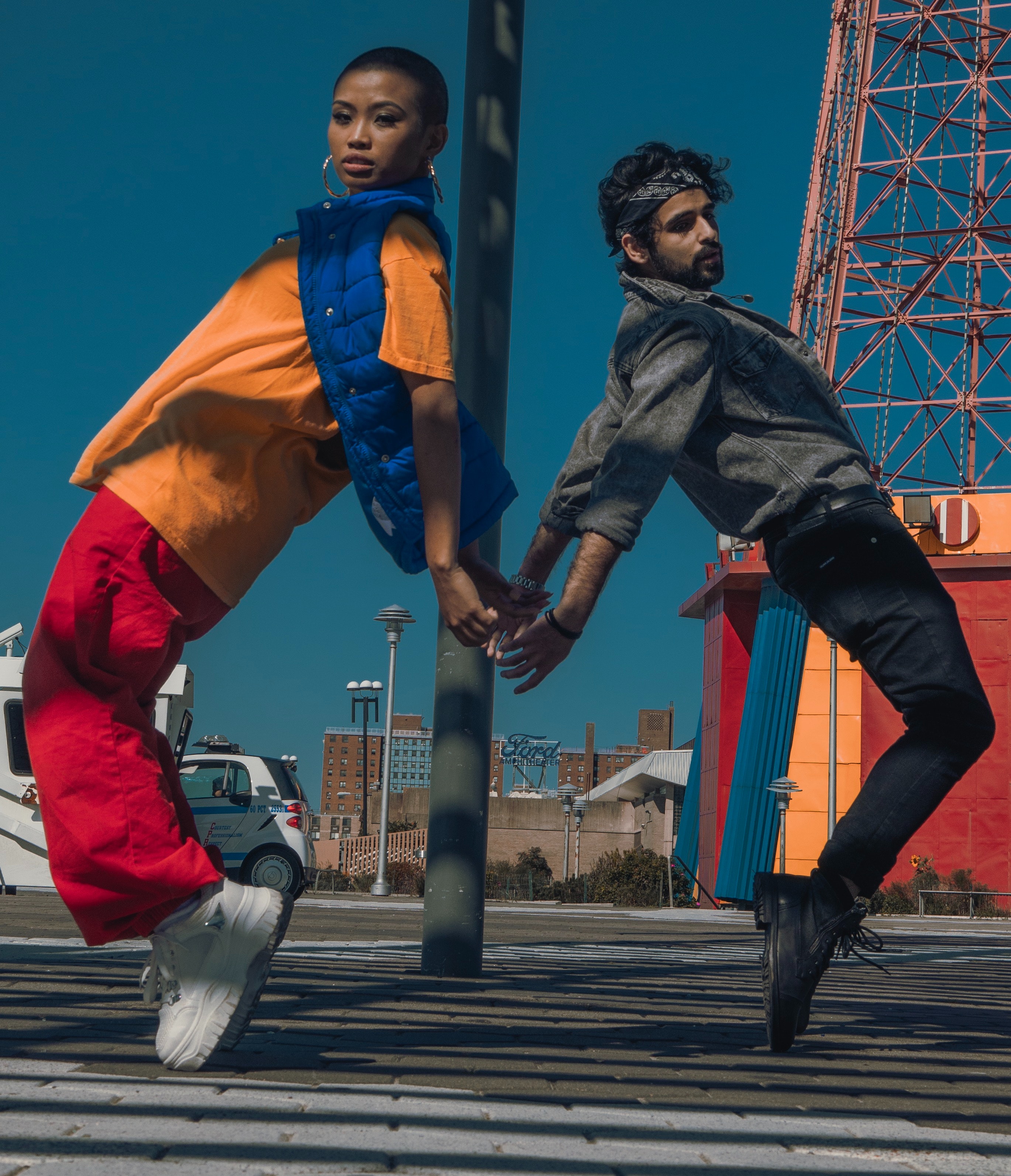 Two people with brown skin in casual street wear joining hands on their tip toes