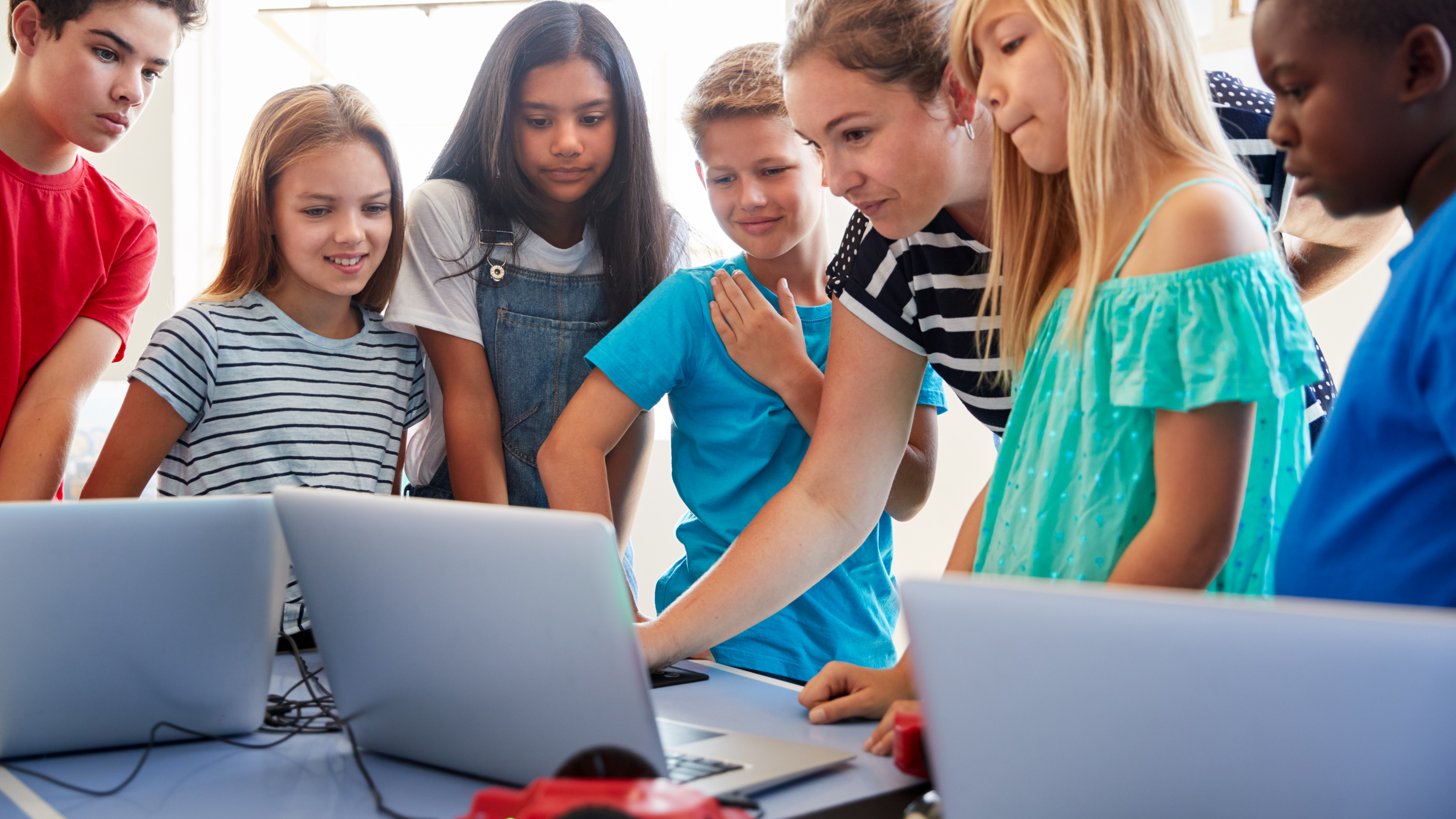 students working with teacher around laptops