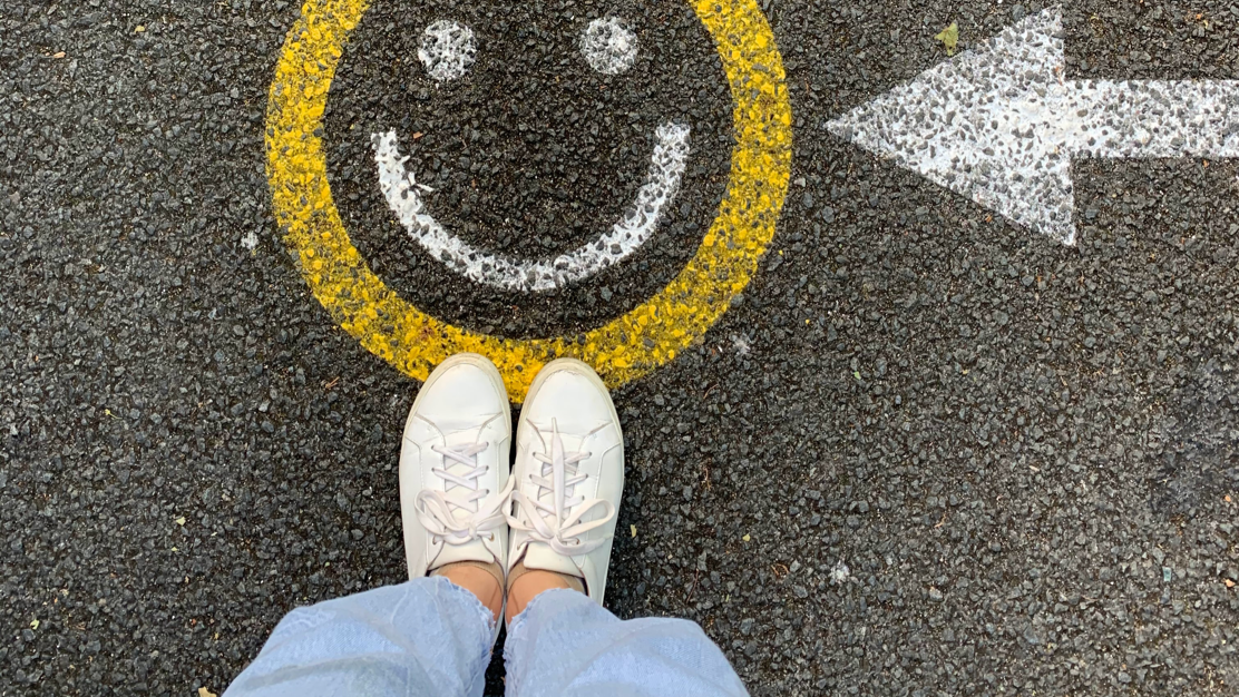 A person&#39;s feet standing on a smiley face drawing