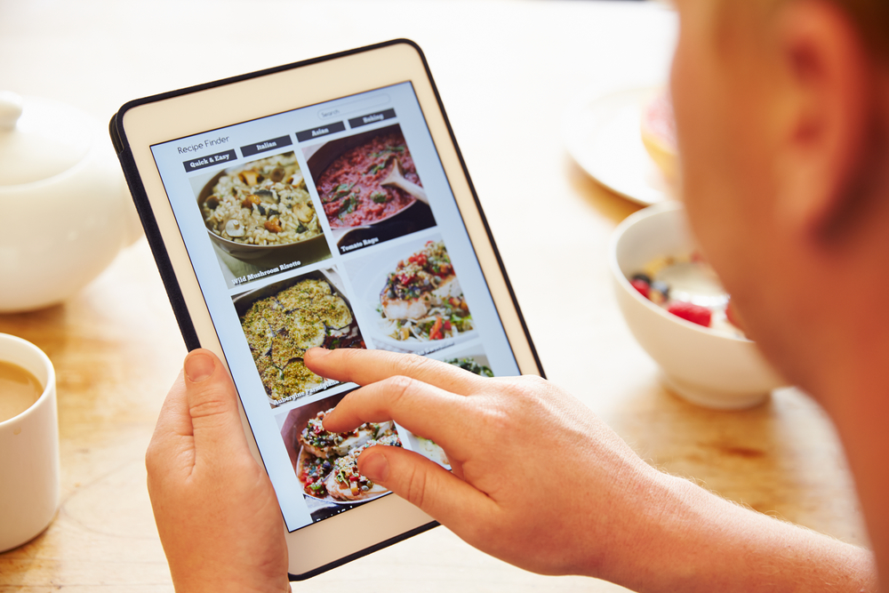 woman looking through recipes on her tablet while she makes a meal plan