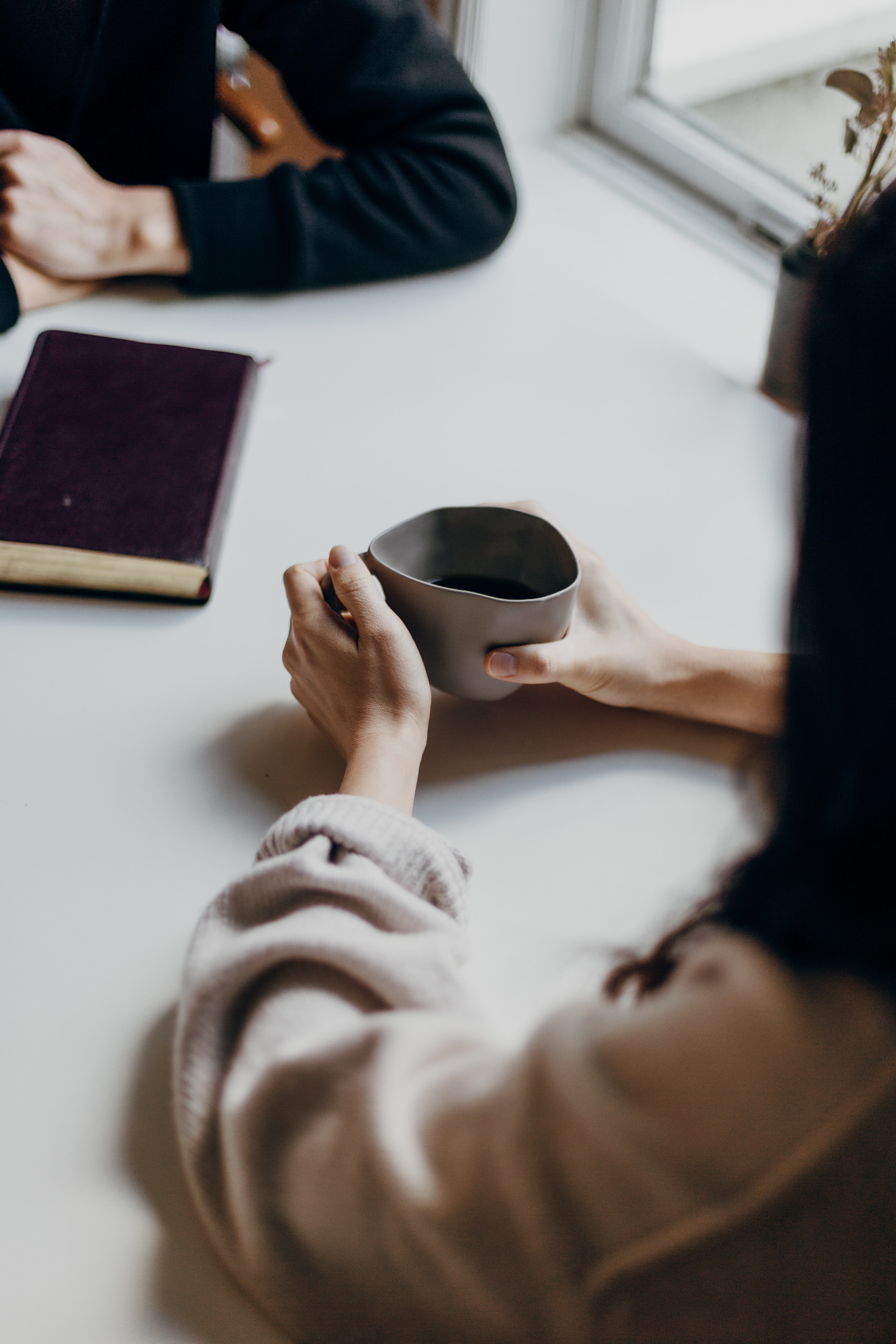 Two people sat at a table talking. One is a women holding a cup of tea. 