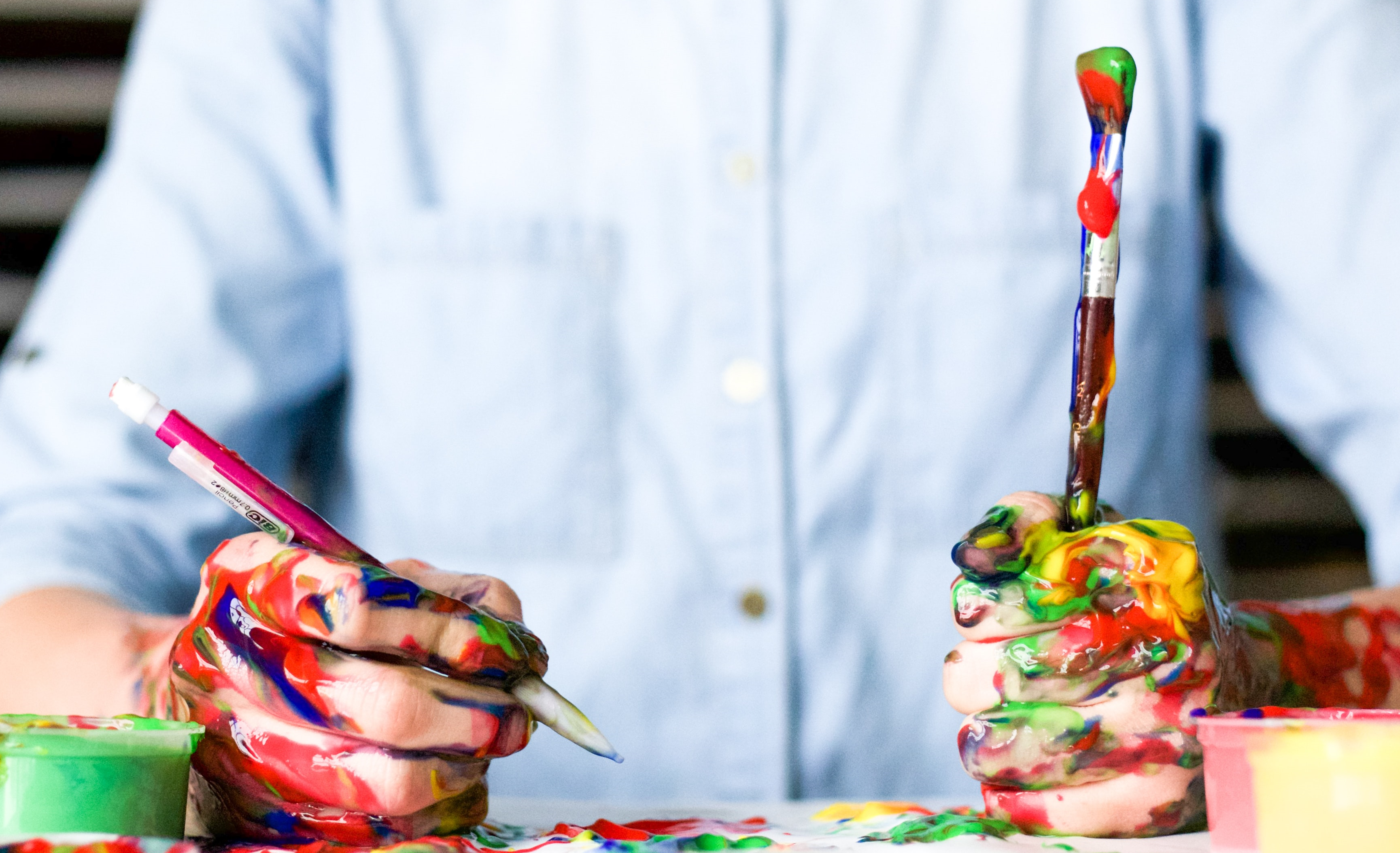 Picture of a man with a paintbrush and pen in hand and with messy paint and ink all over their hands and arms