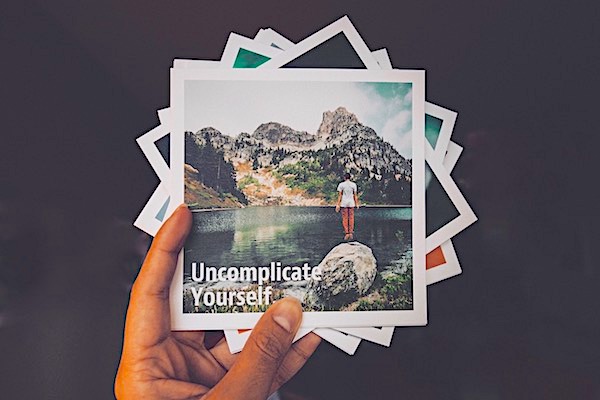 Hand holding a pile of photographs with the words &#39;Uncomplicate Yourself&#39; written on the top one