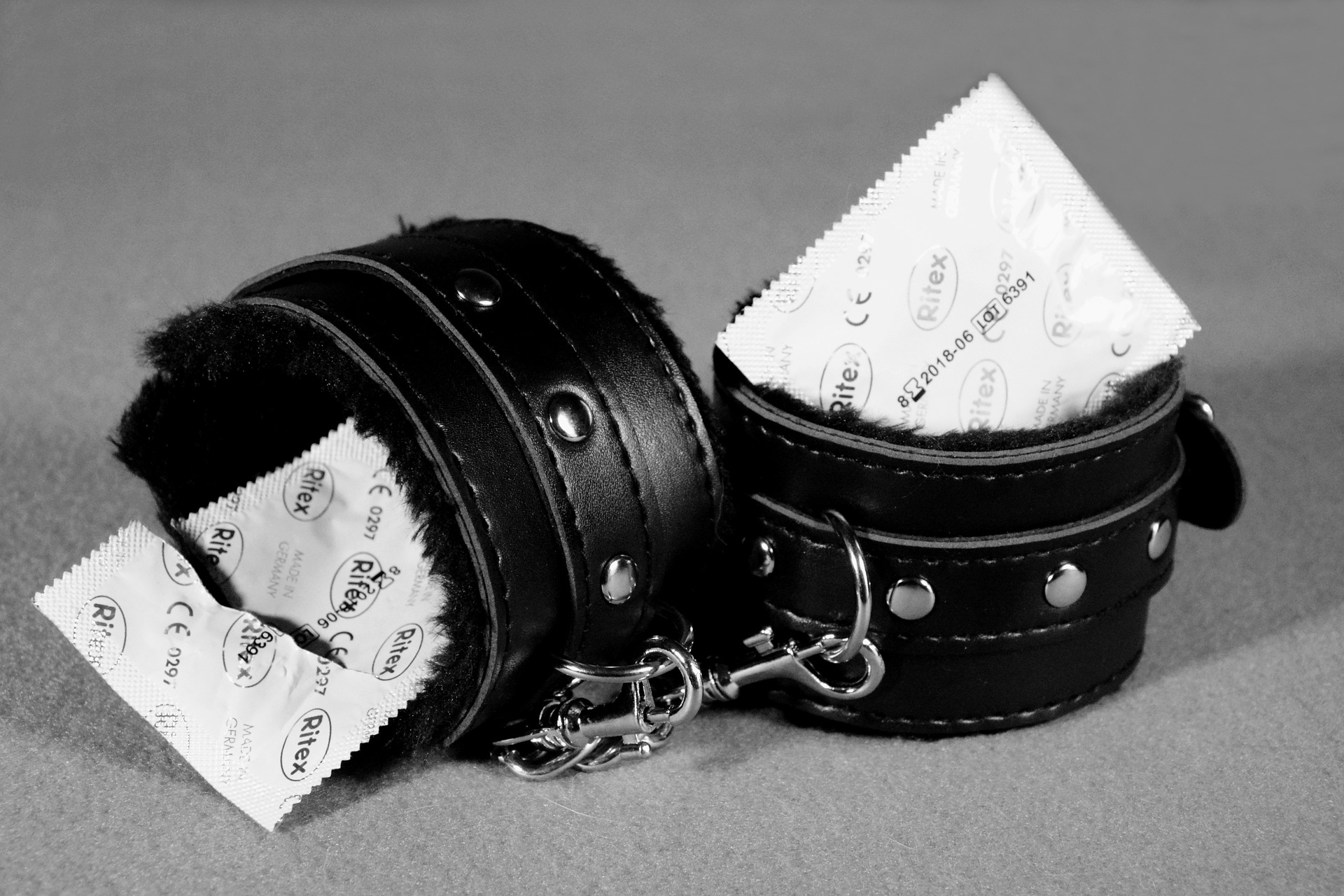 Black leather fur-lined cuffs against a gray background with a condom packet tucked into each cuff