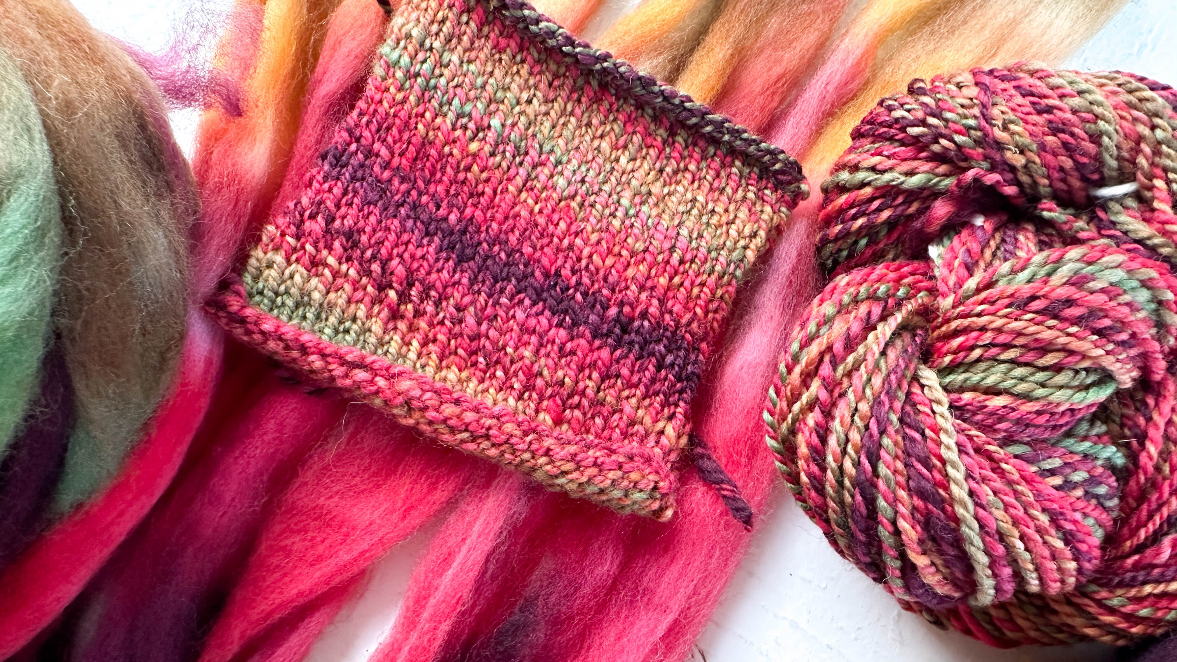 A selection of wool roving, handspun yarn twist, and a knitted swatch highlighting color variations in shades of red with green and yellow flecks