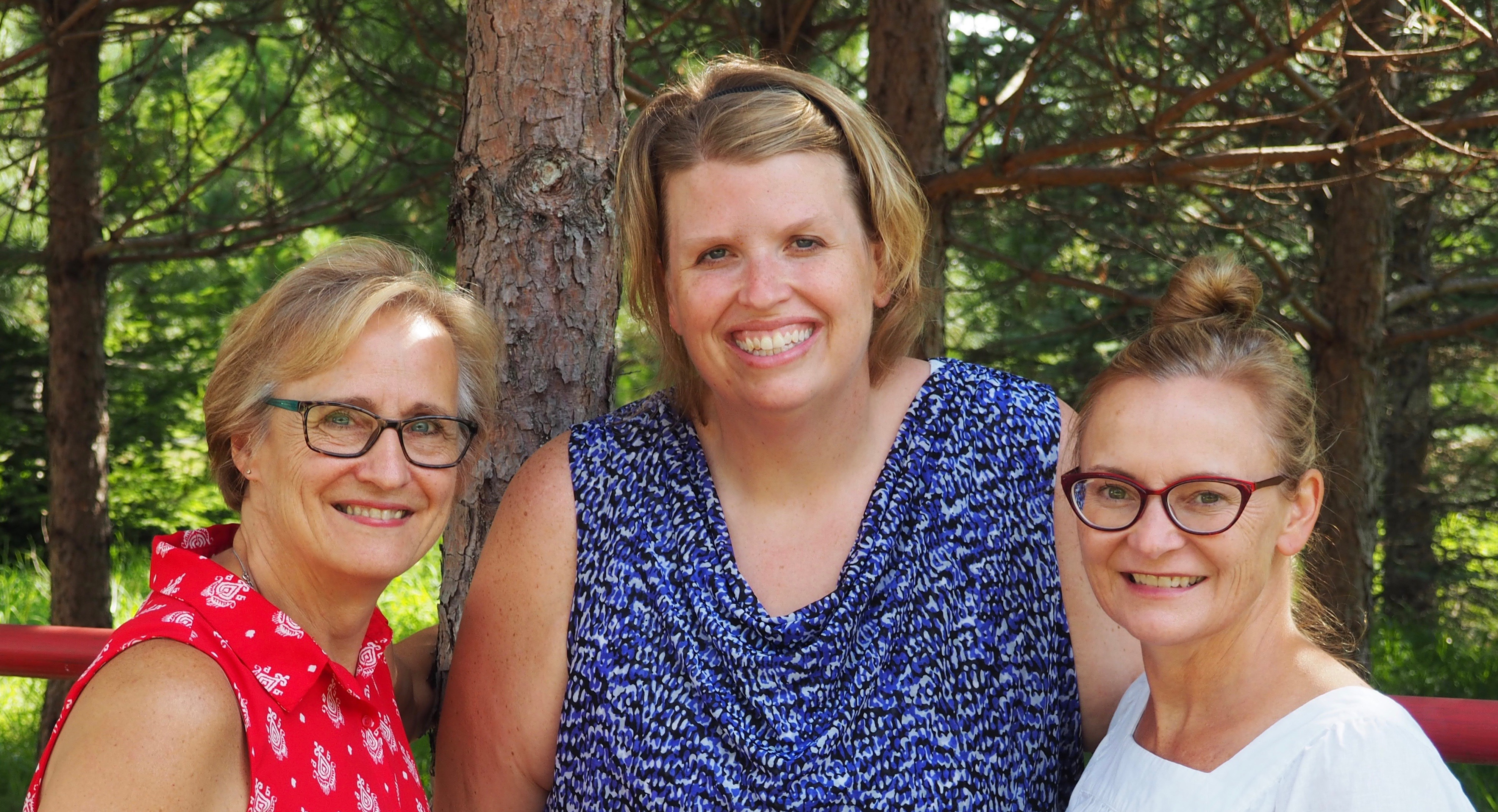three women standing by a pine tree