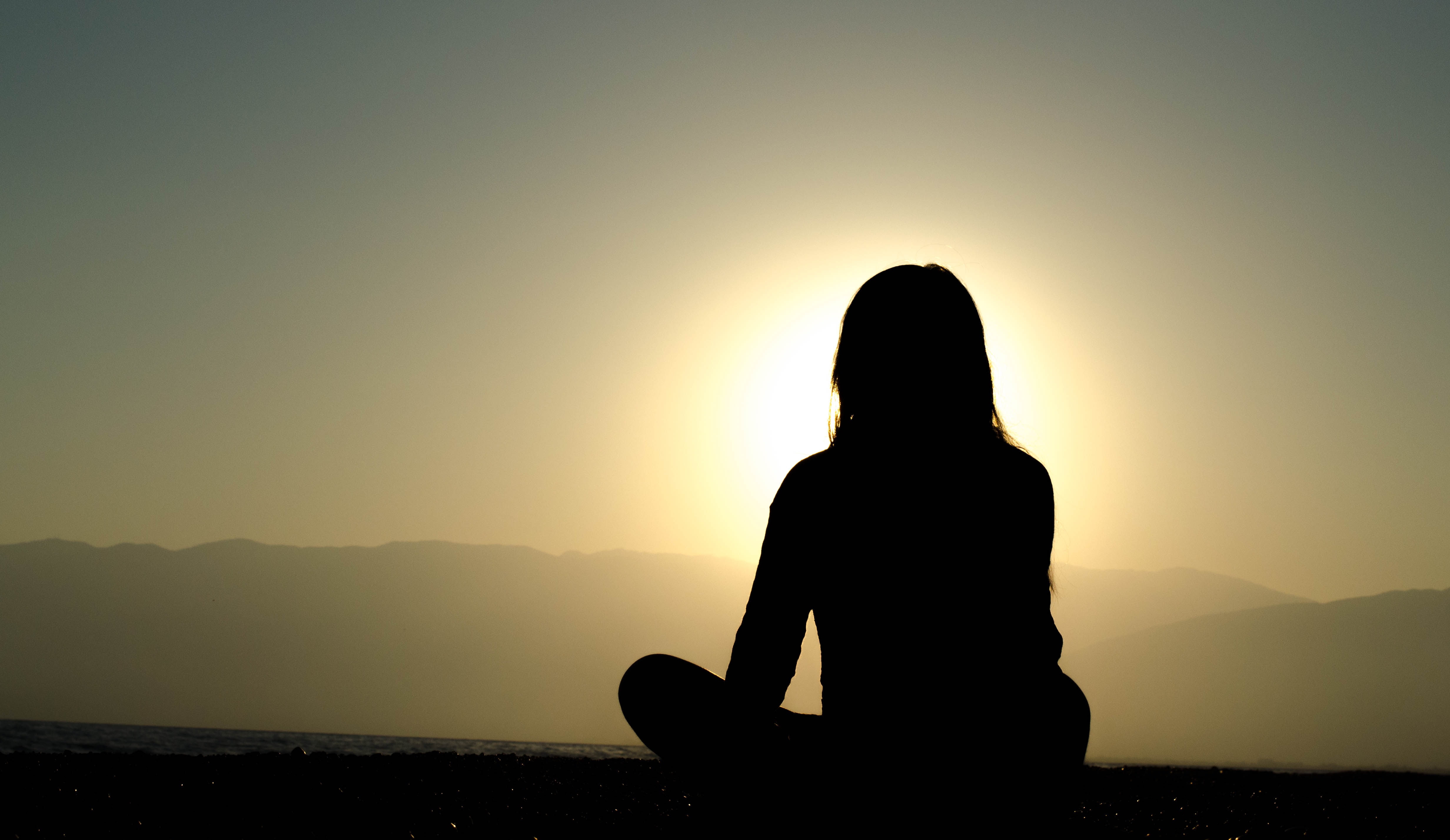 Silhouette of a lone woman looking at the sunset over mountains