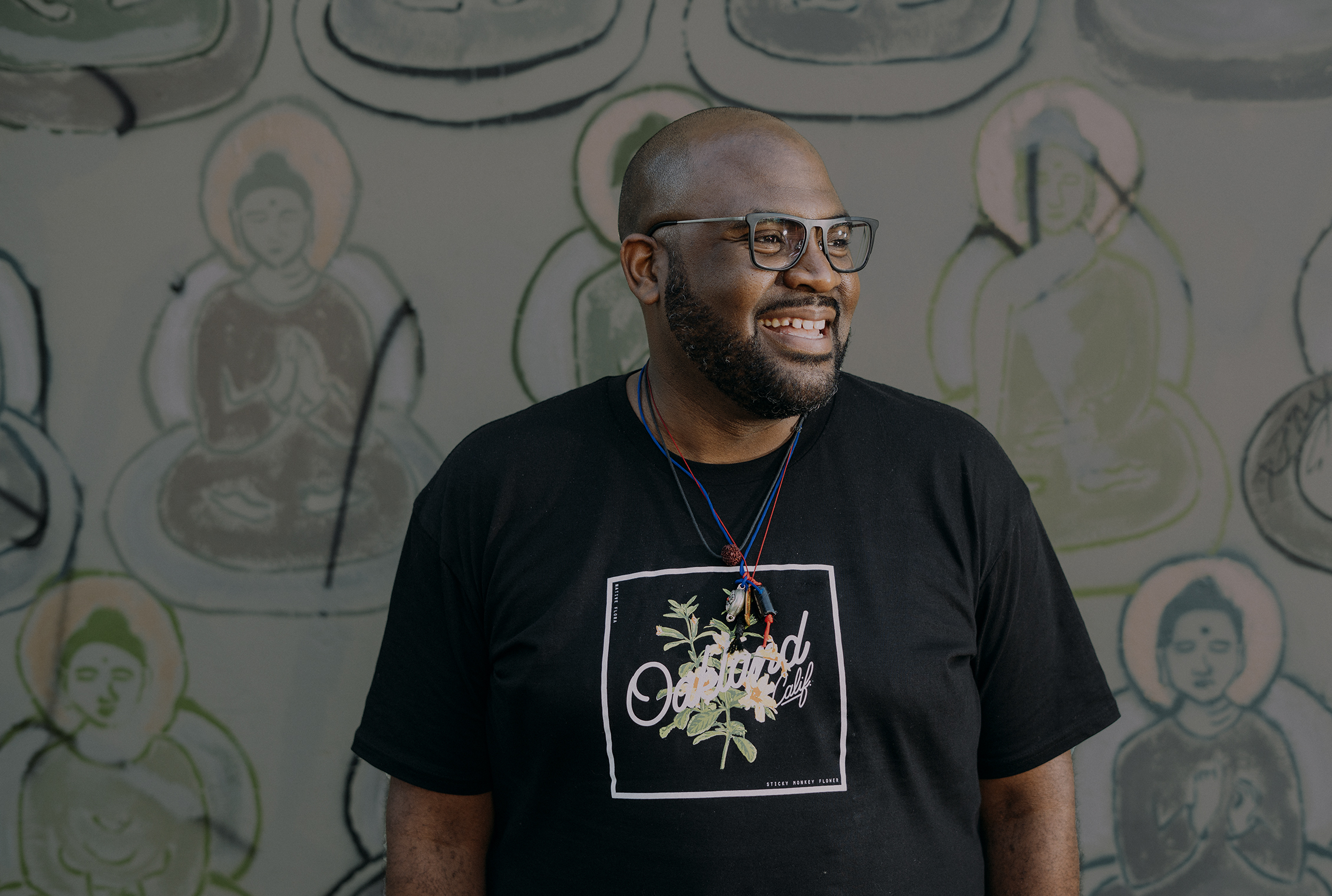 A photo of Lama Rod Owens in front of a wall with buddhas painted on it