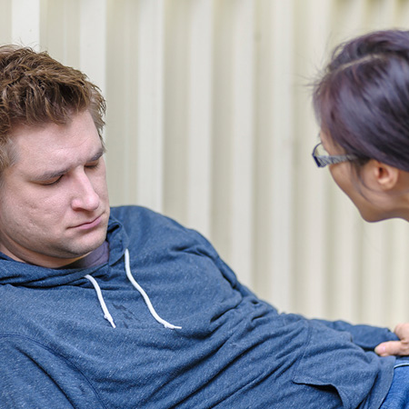 A person with their hand on the arm of another person with a greyish complexion who appears unconscious.