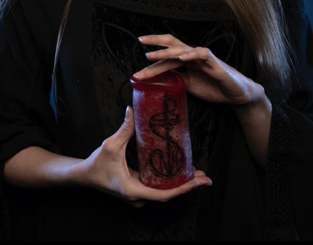 hands holding a red candle with a black treble clef carved into it