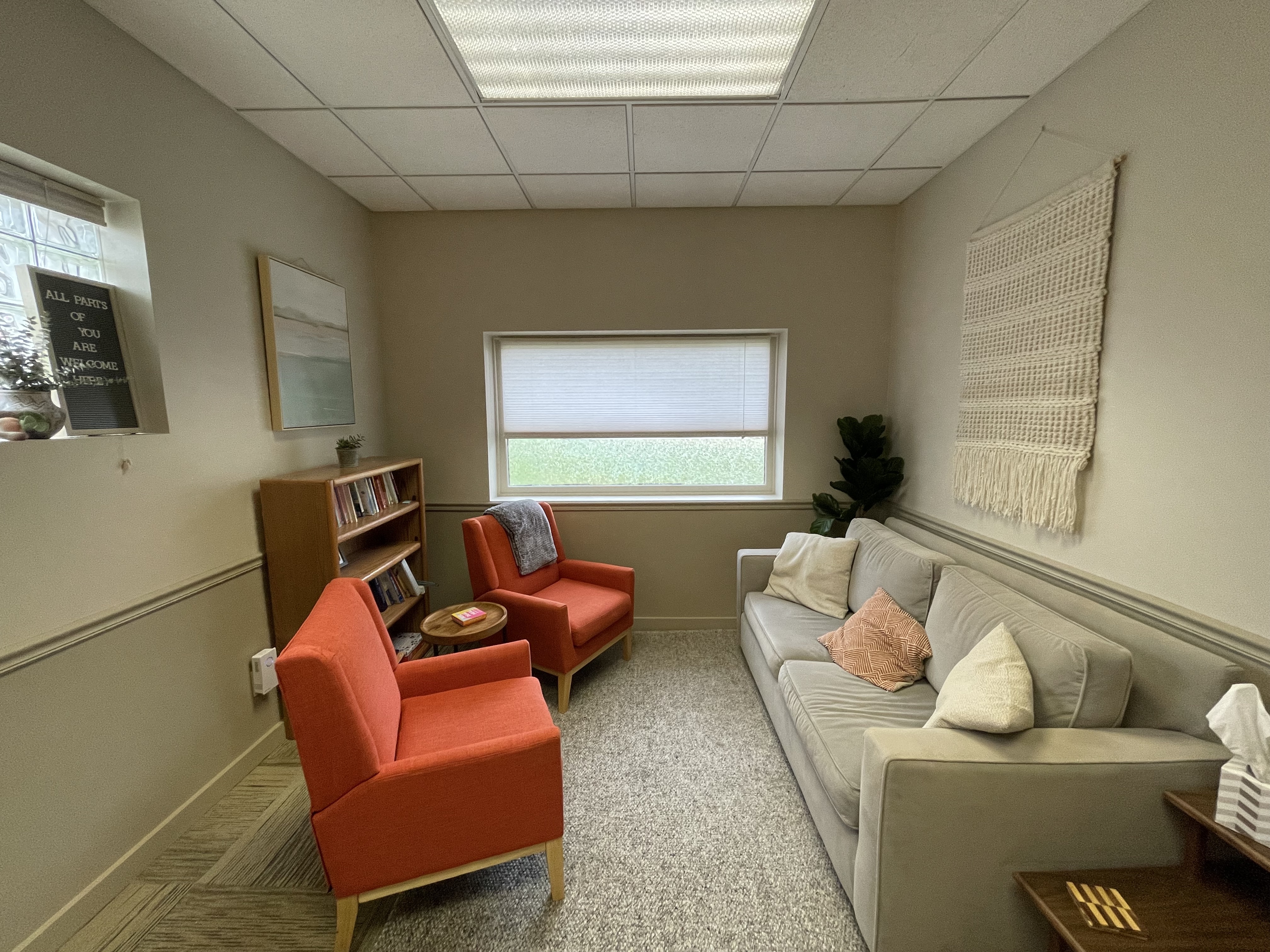 Image displays a traditional therapist office. On the right of the images is a beige couch, and on the left includes two orange armchairs with a table in the middle.