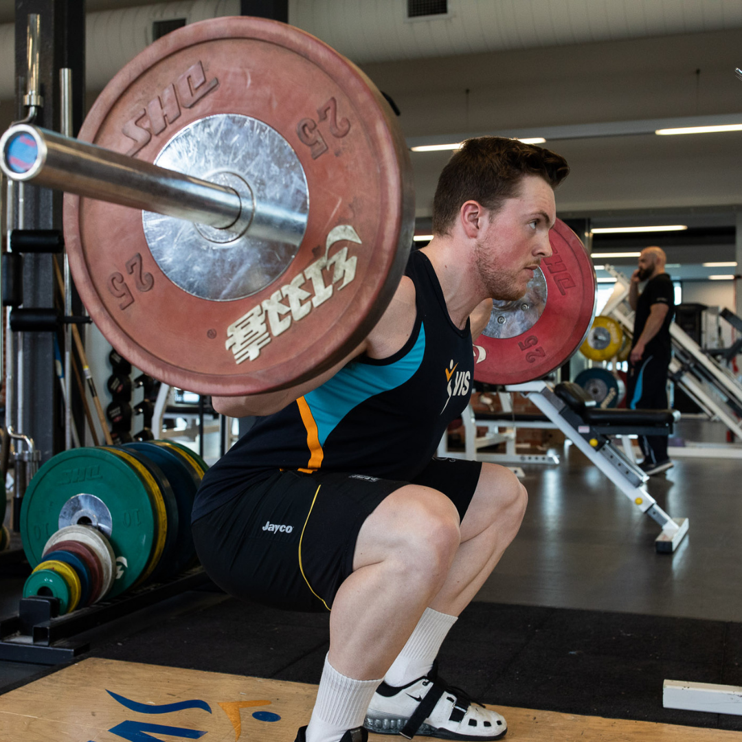 Man squatting a barbell to improve quad strength in acl recovery.