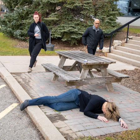  A person lies unconscious near a picnic table; two people approach her quickly.