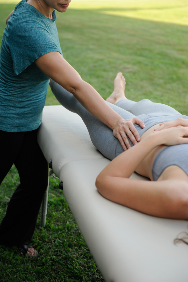 Female massage therapist massaging left hip of a reclined woman wearing grey athletic clothing