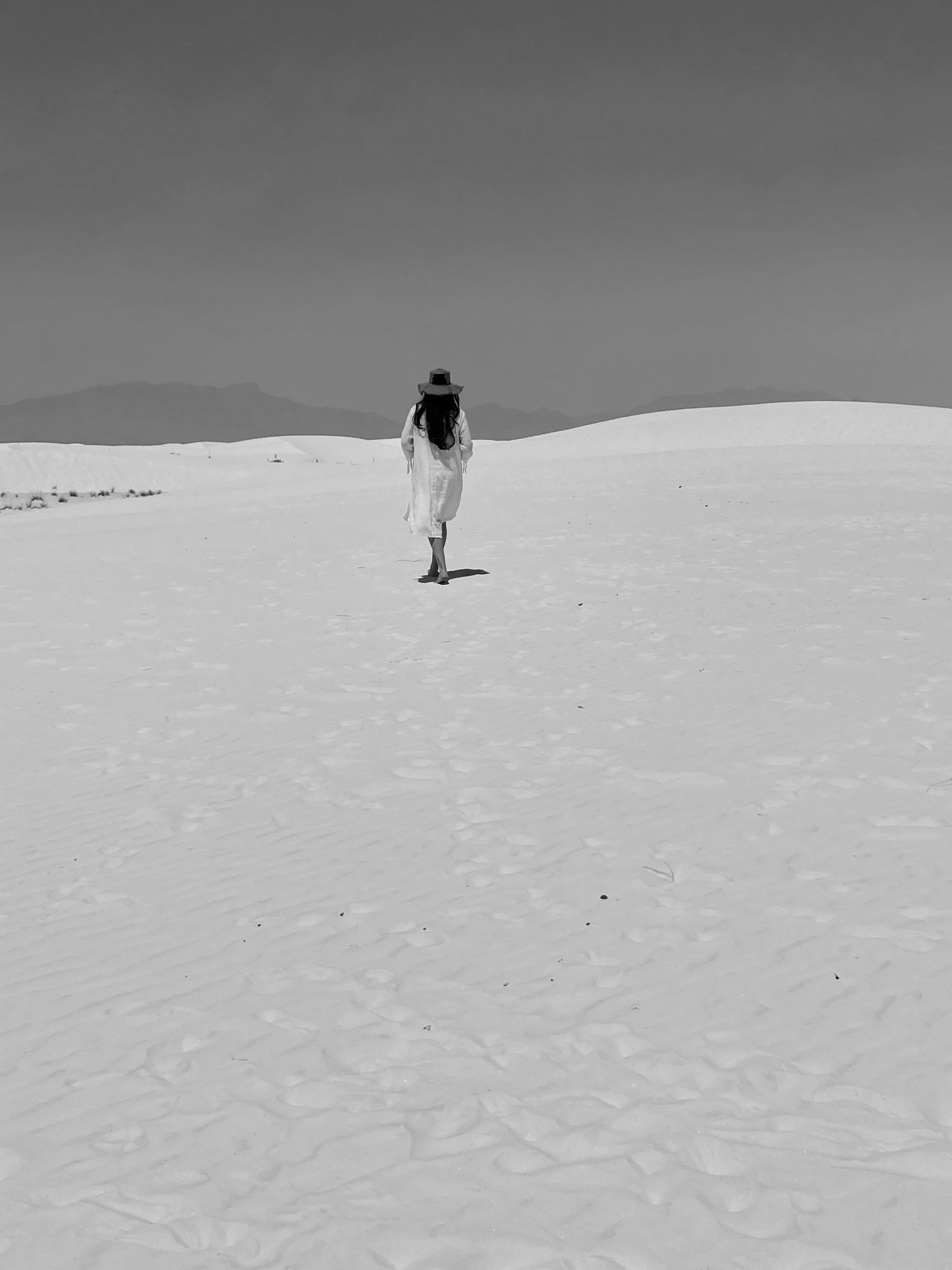 Woman in white dress with hat walking in desert