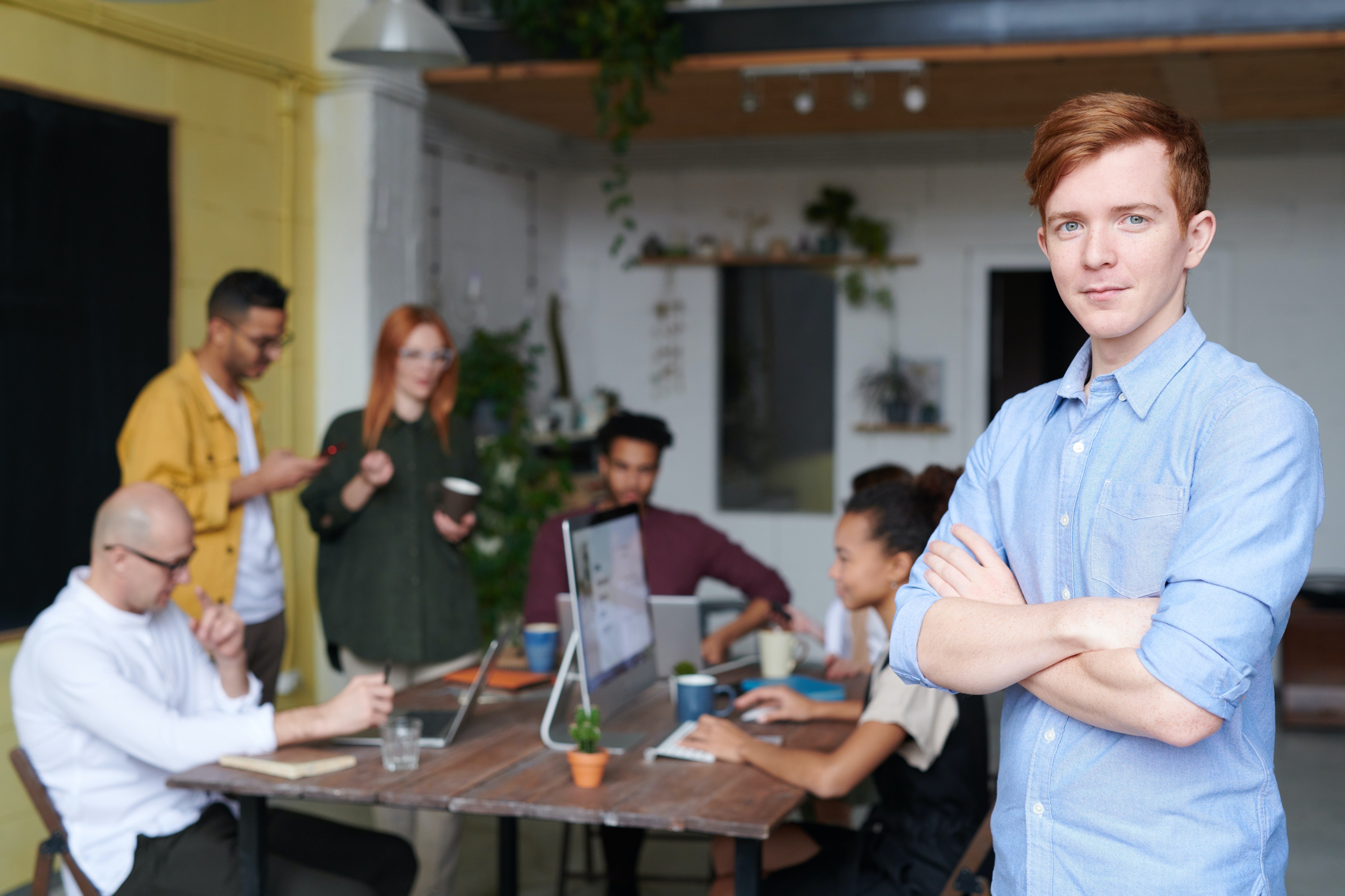 Man standing with folded arms in front of team working