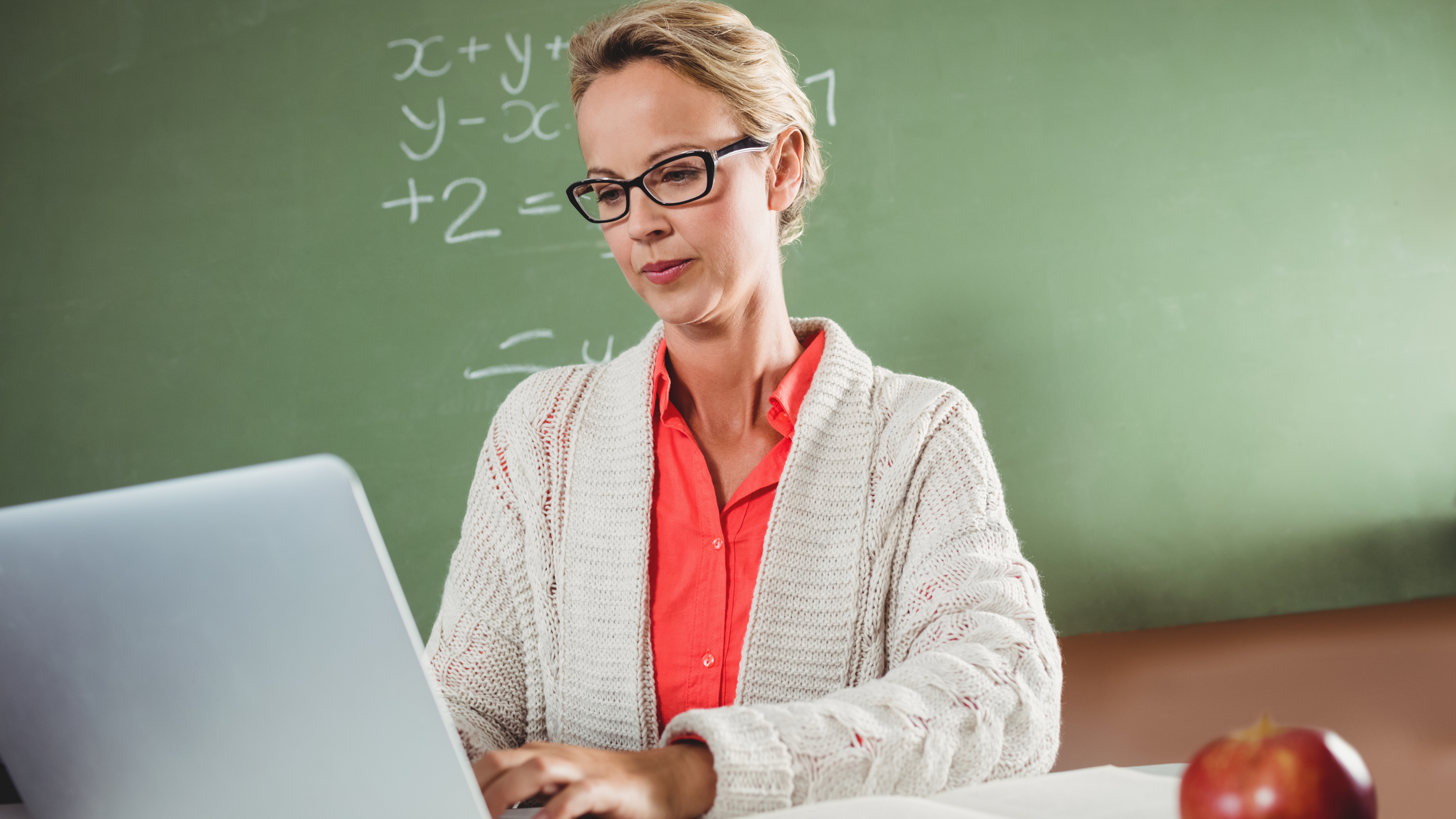 woman wearing glasses using laptop in front of chalkboard