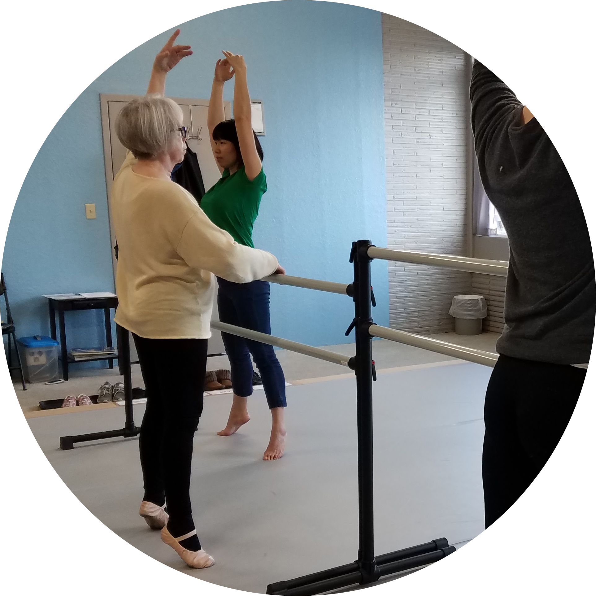 Two adult ballet students balance in first position on demi-pointe at a ballet barre at Find Your Center's studio