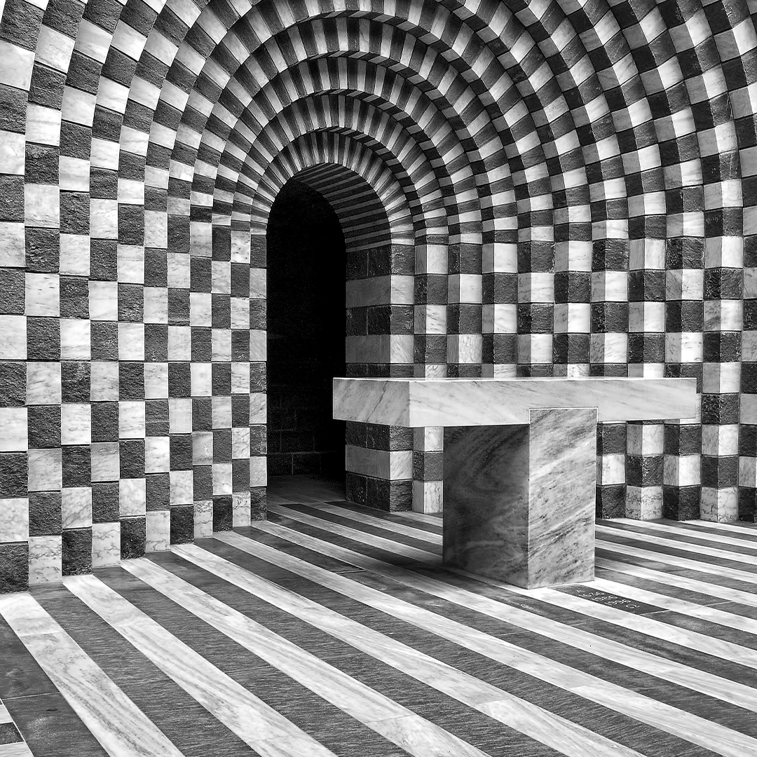 Room with grand architectural elements and stone table leading to an arched doorway 