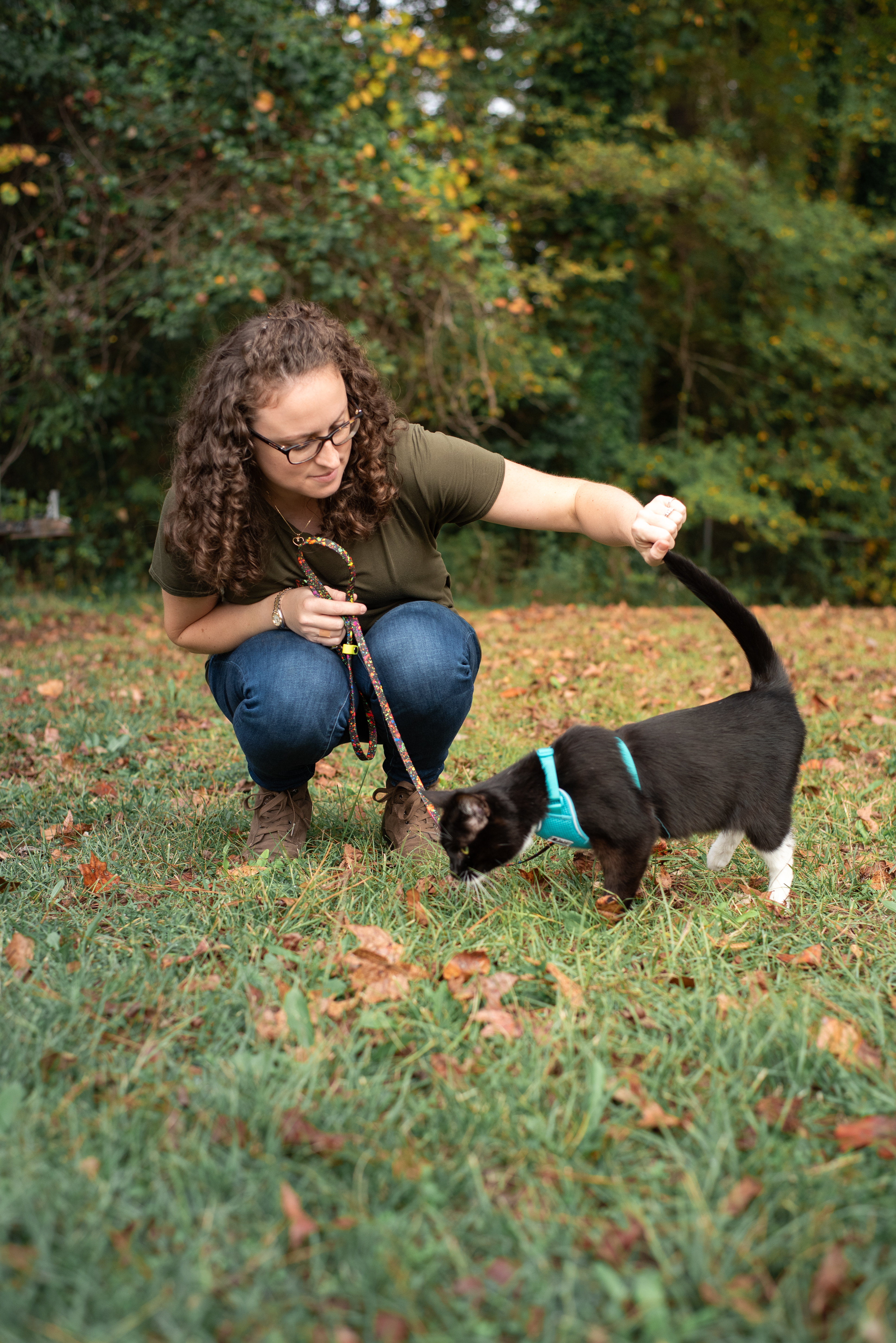 woman outside bending down to pet a black cat on a harness and leash