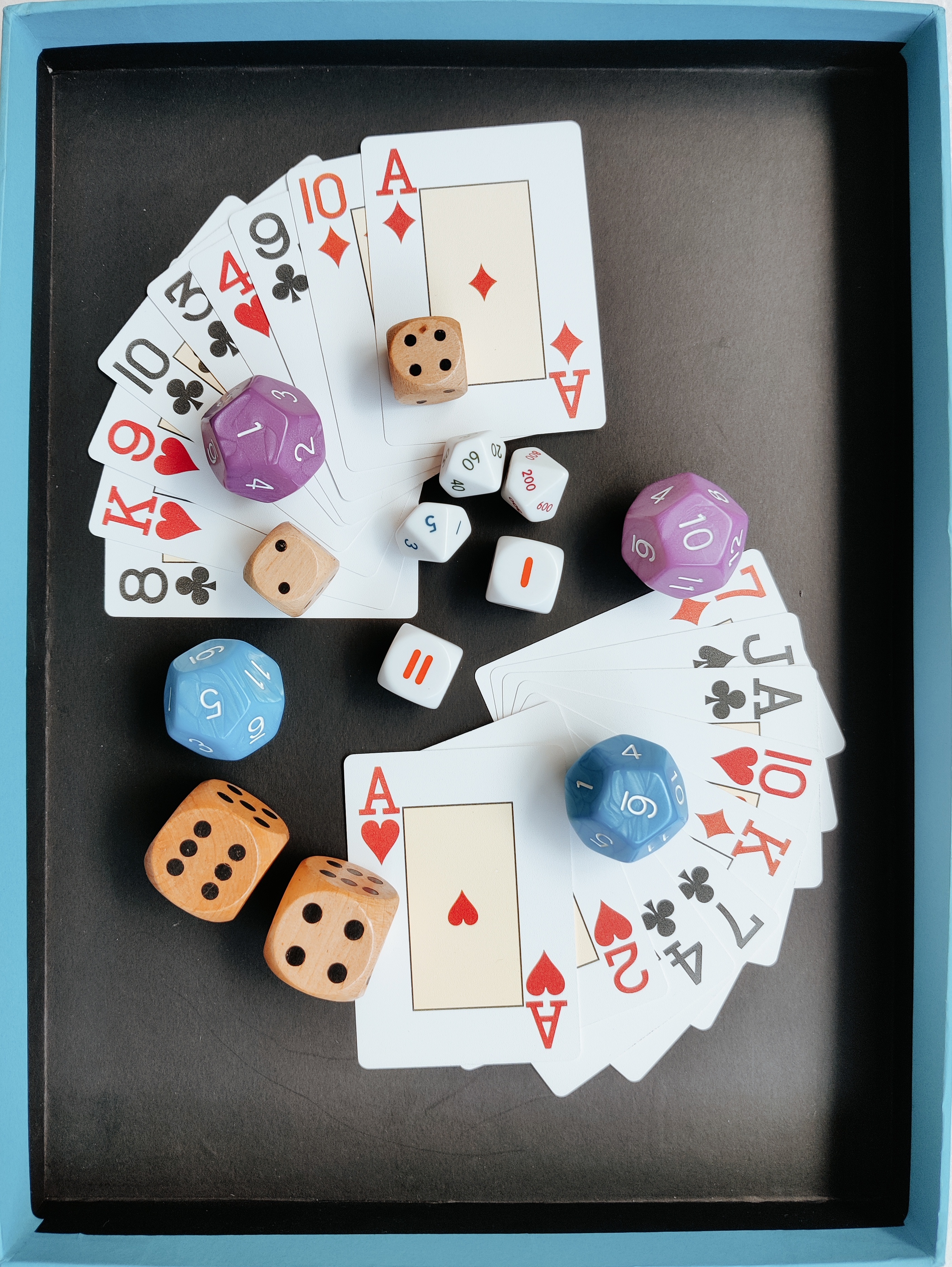 Playing cards and different types of dice laid out on a black background with a blue border