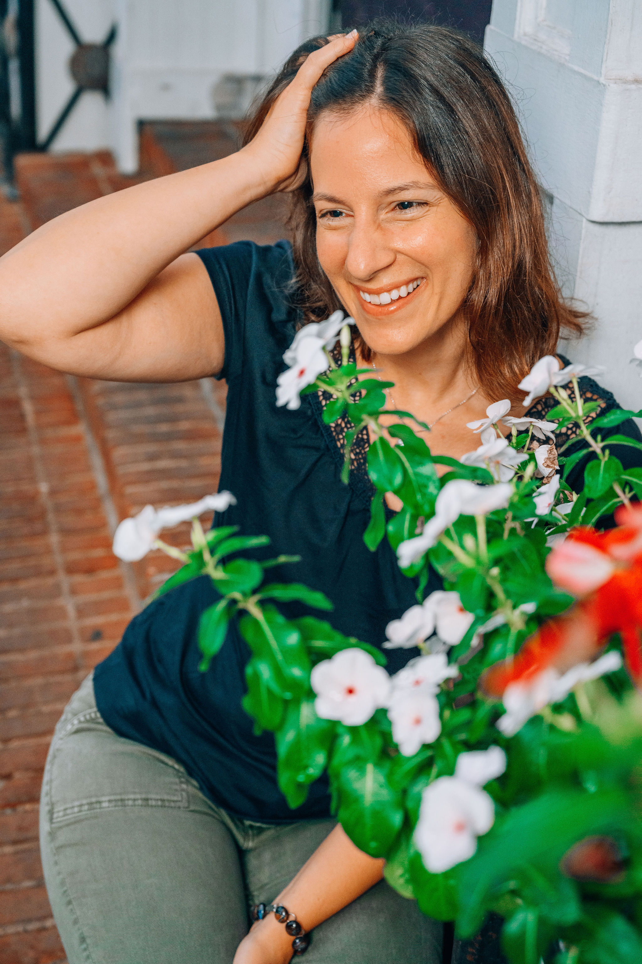 Photo of Emily smiling, pushing her hair back with her right hand. There are white and red flowers in the corner of the image.