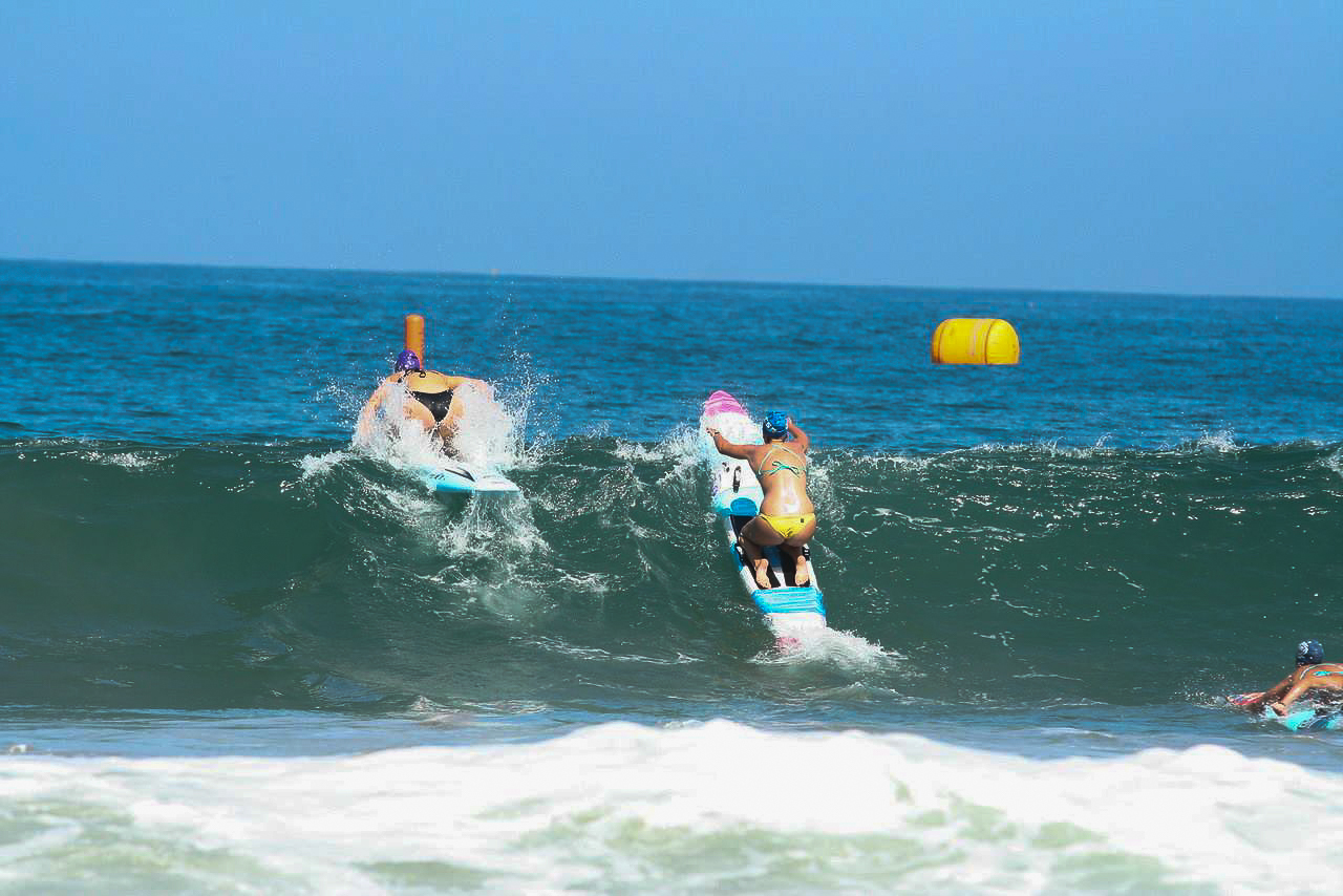 two lifeguard racers paddling over a wave