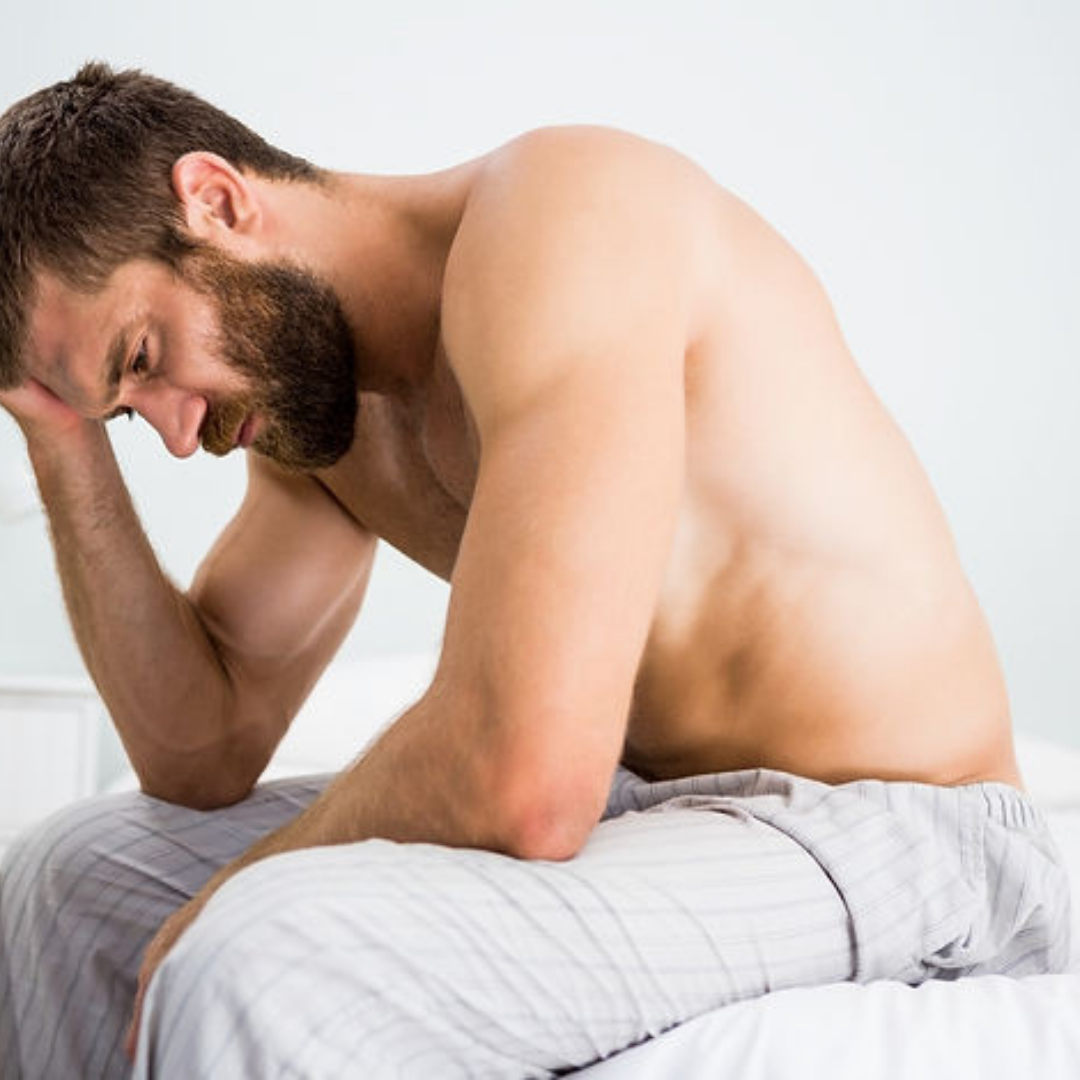 Frustrated man sitting at edge of the bed with head in his hands
