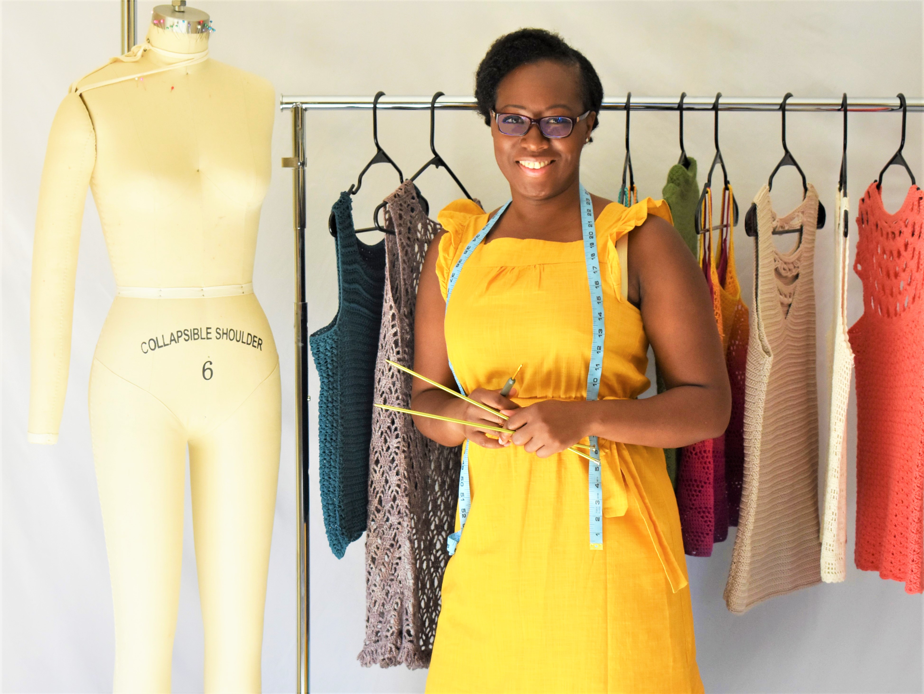 Woman standing in front of dress form with knitting needles and crochet hook. 