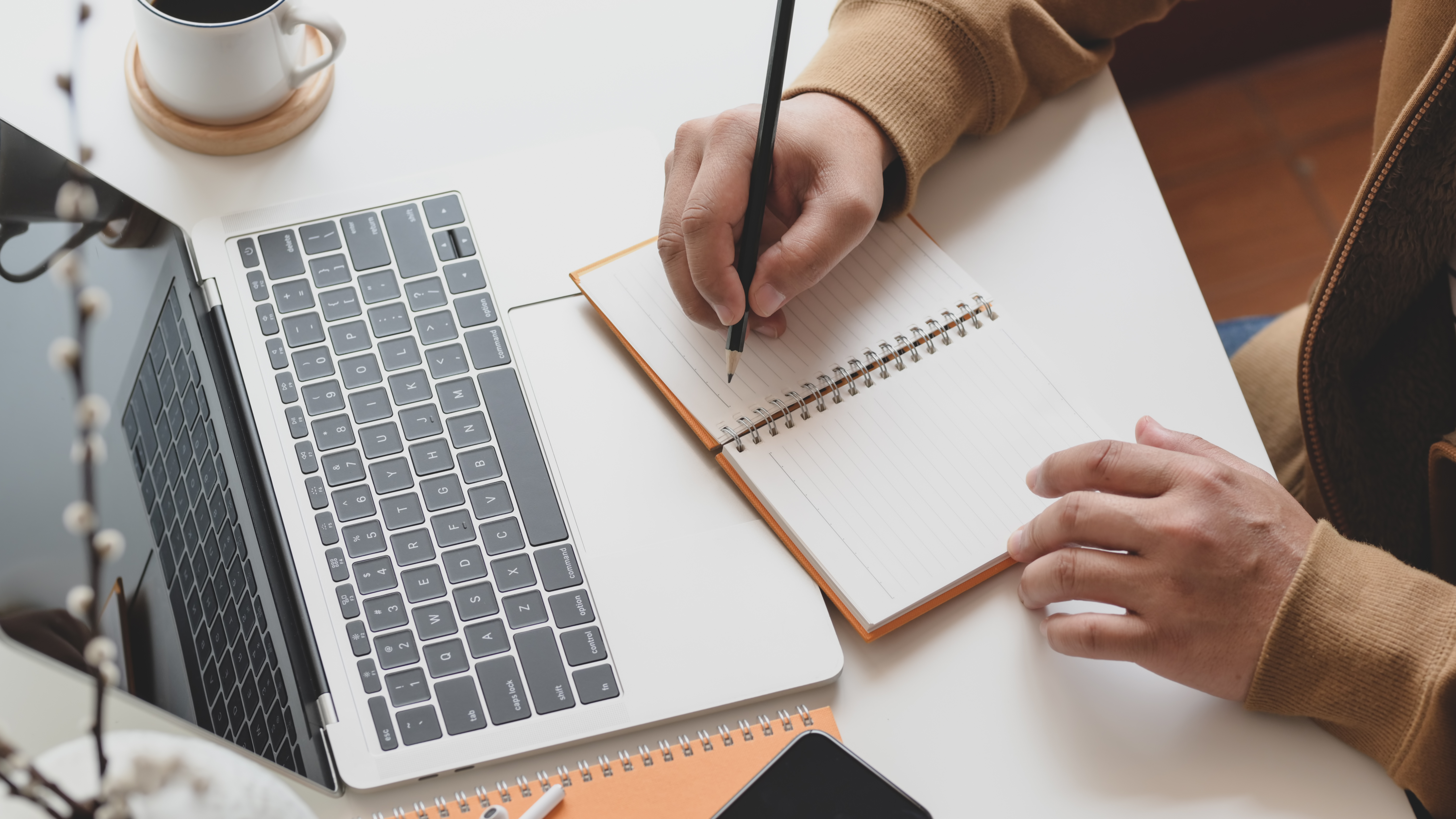 person writing in a notebook in front of an open laptop