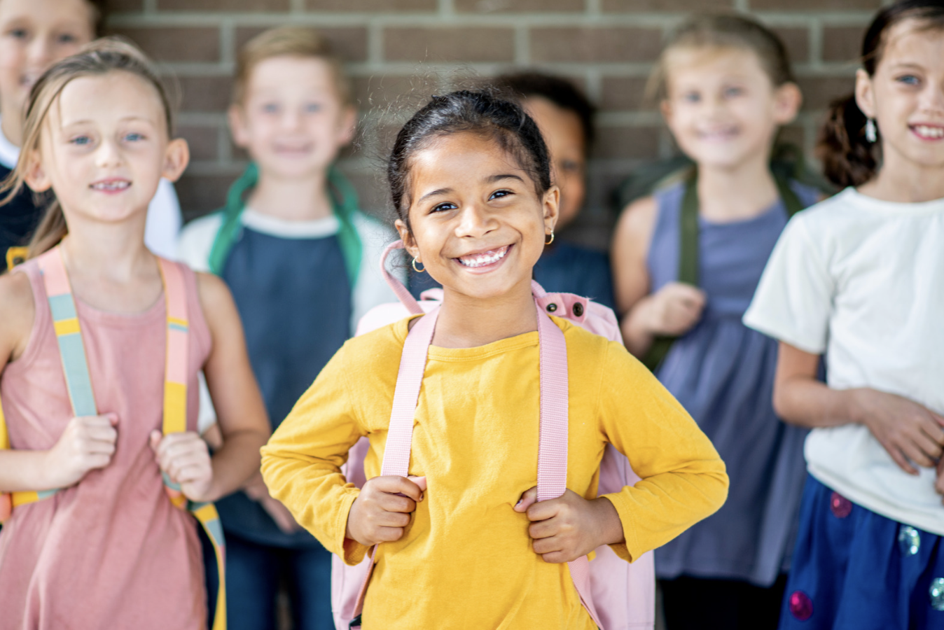 A smiling young child stands smiling amongst othr children of the same 