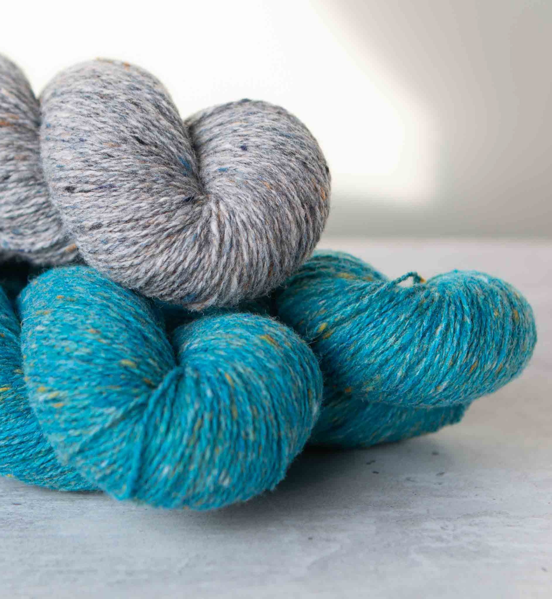 Pile of three skeins of Darnie yarn, two in a blue shade and one in a grey shade. 