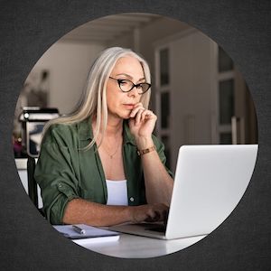 woman looking carefully at laptop with notepad and pen next to her