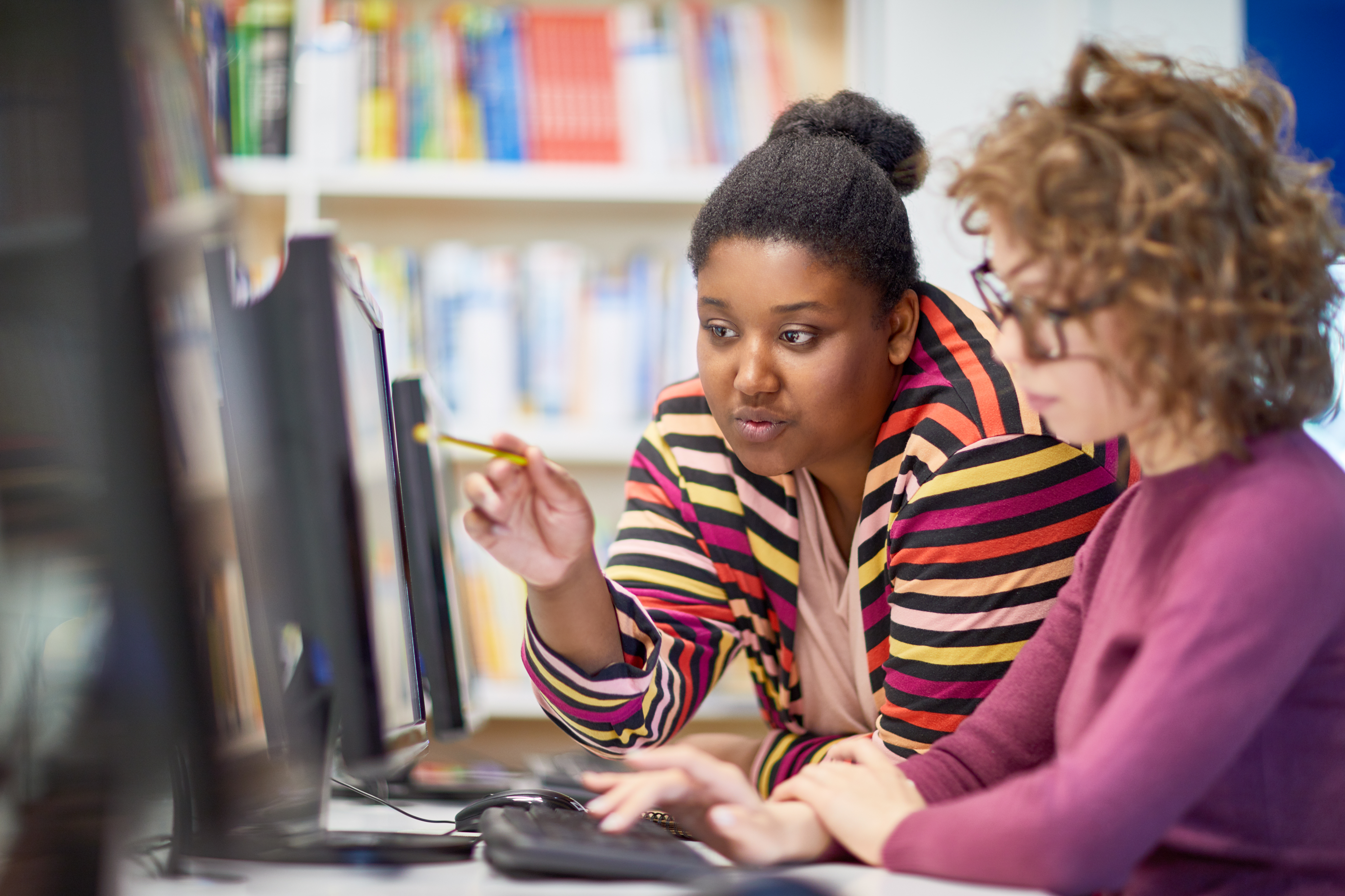 Teacher leans over keyboard as student works on a computer