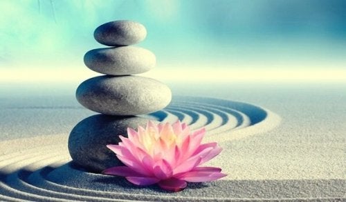 Stacked rocks in sand with pink flower at base