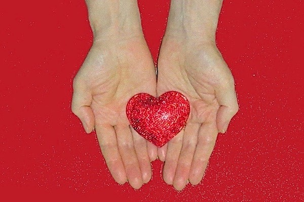 Red heart shape held in two hands cupped together with their palms upwards