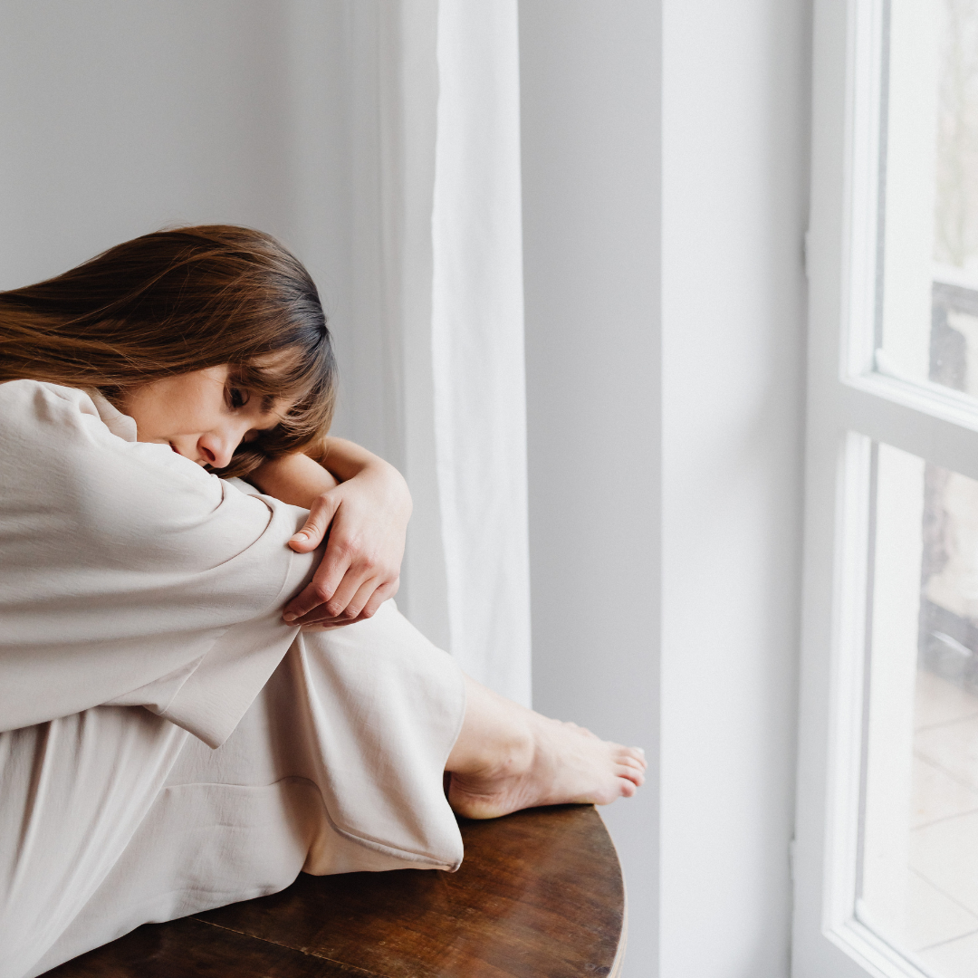 Sad woman sitting down hugging her knees, resting her head on her knees