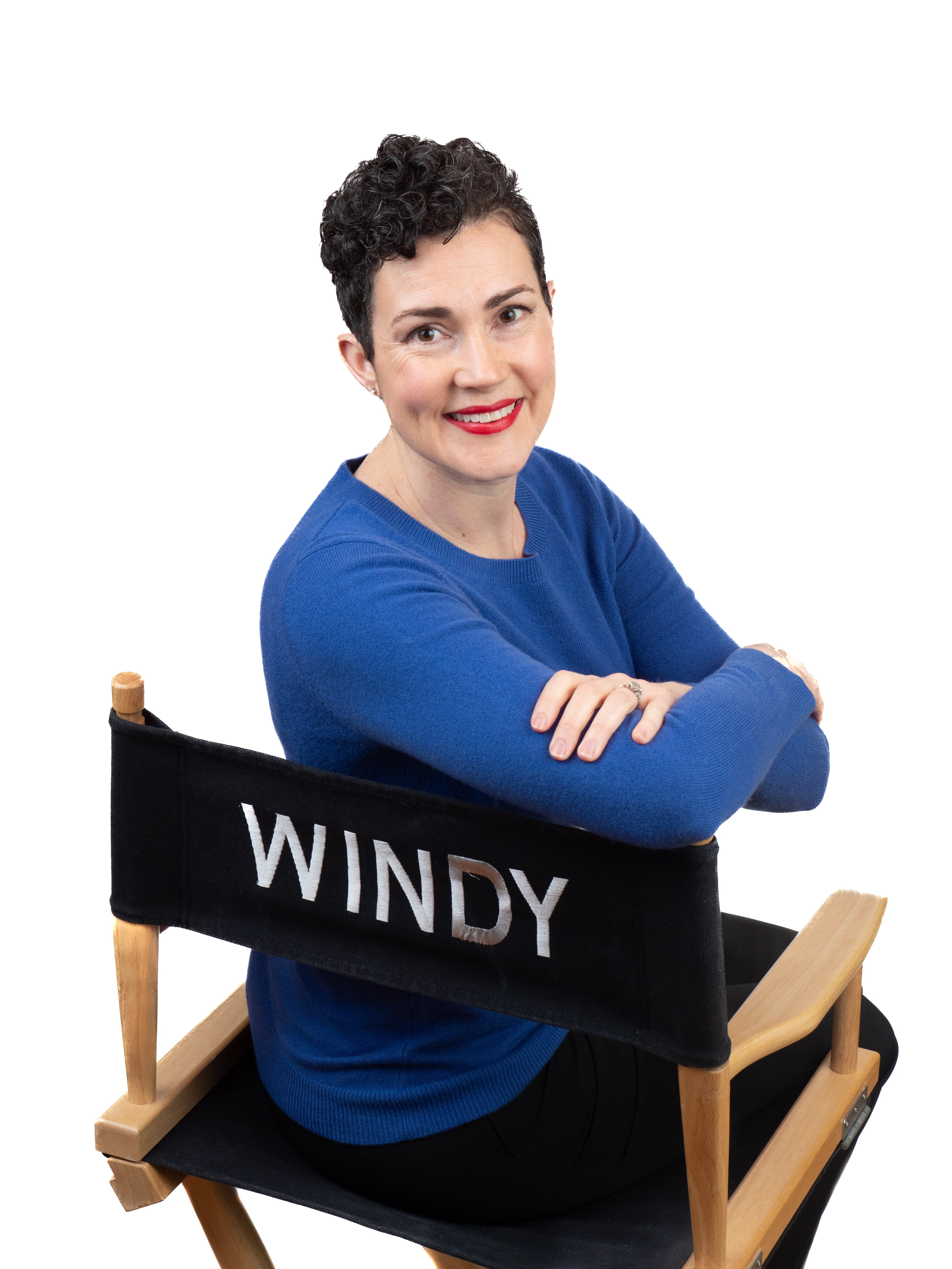 Dark-haired woman in a blue sweater sits in a director chair with the name Windy on it