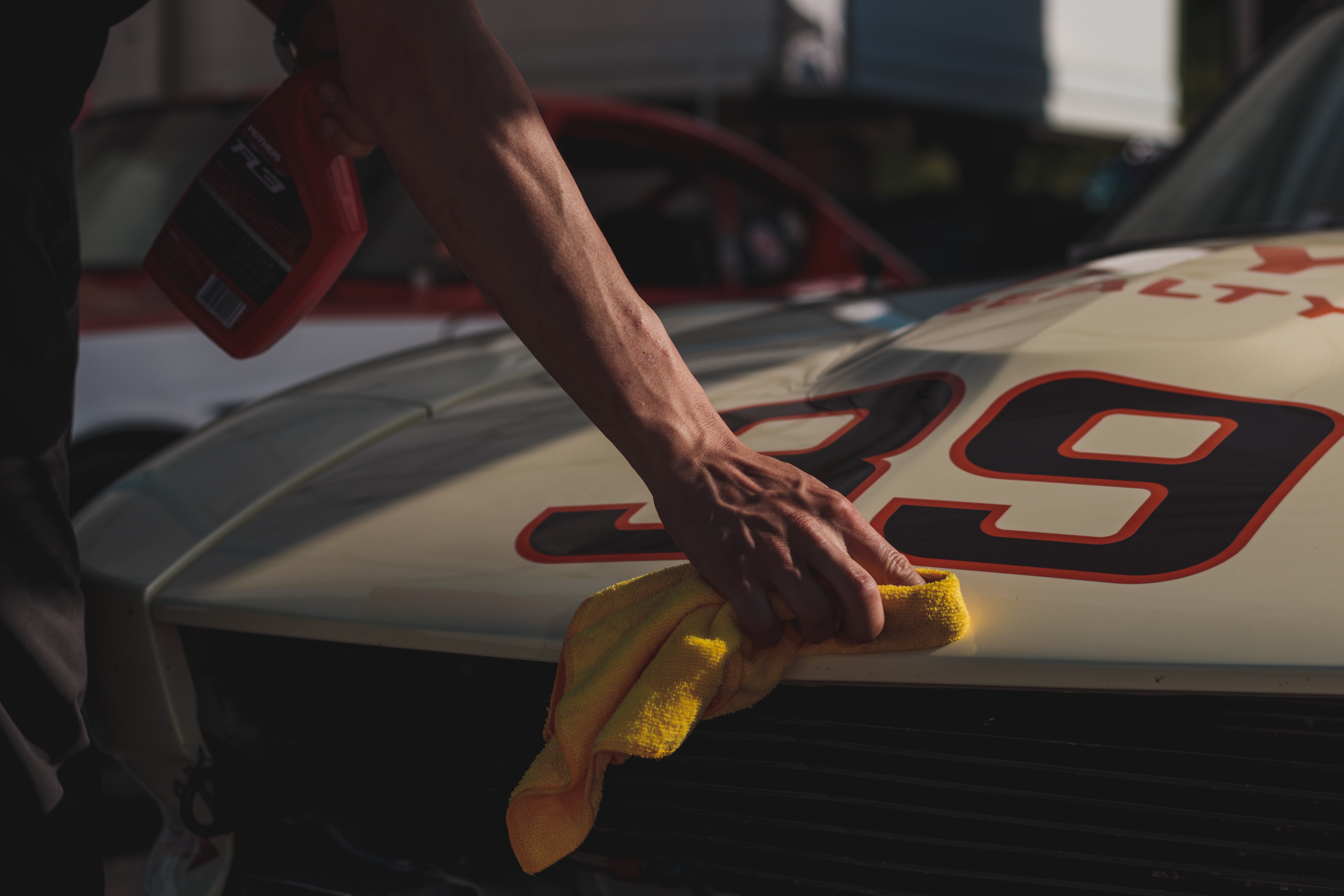 A man applies a finishing coat of polish to the hood of a race car.