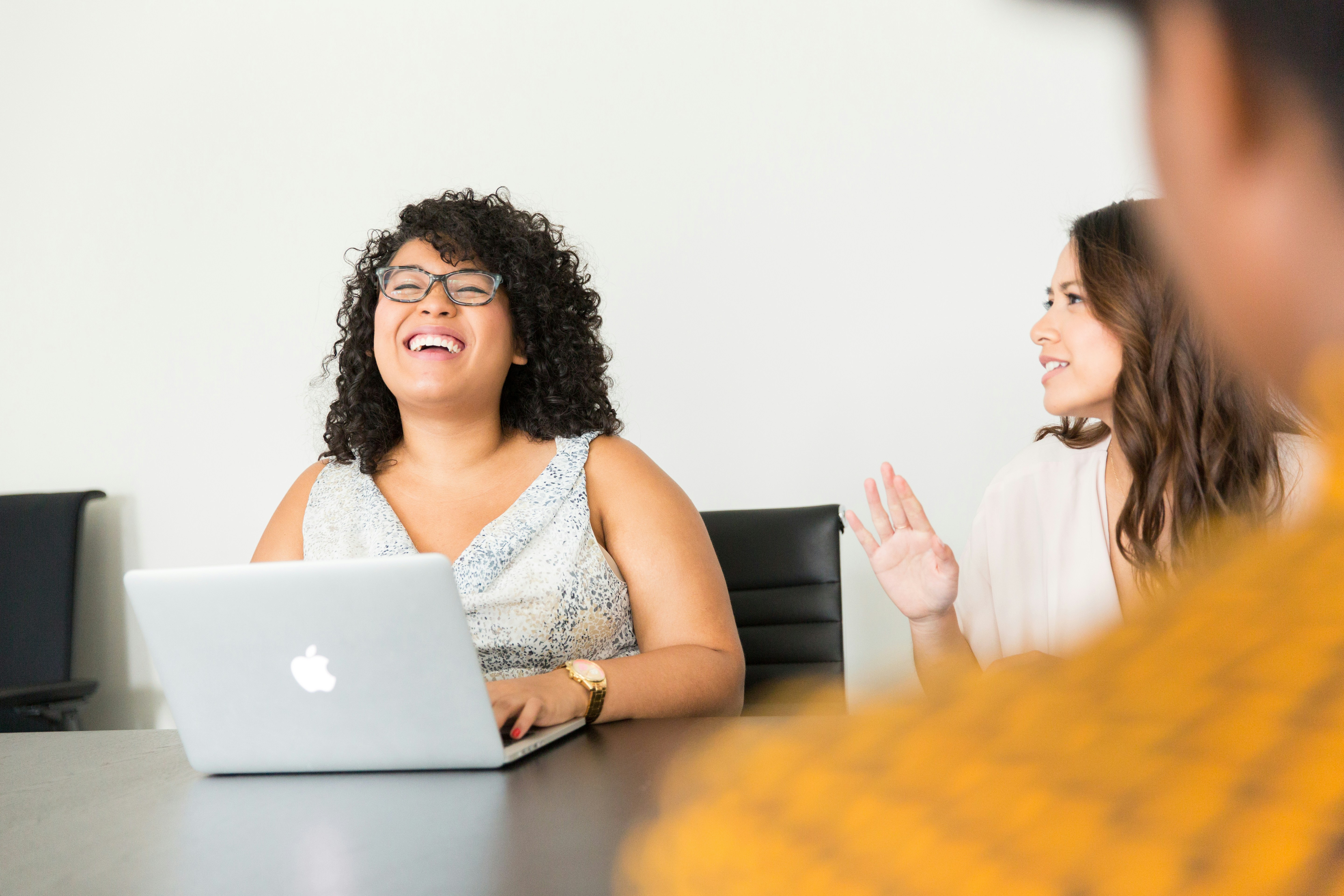 Young woman looking at the laptop screen and laughing while her friend tells a story 