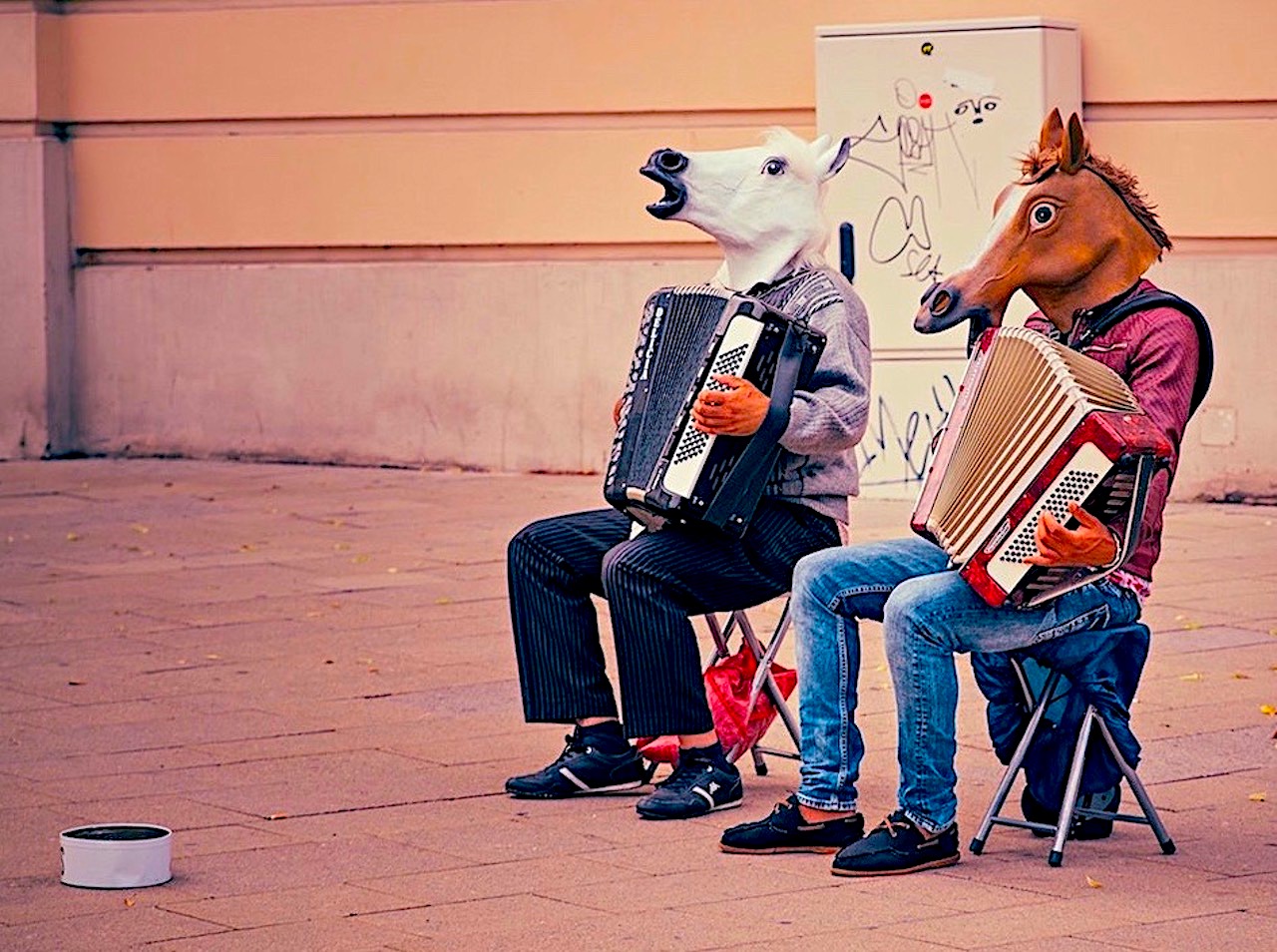 Two people playing accordions sitting on chairs wearing horse heads