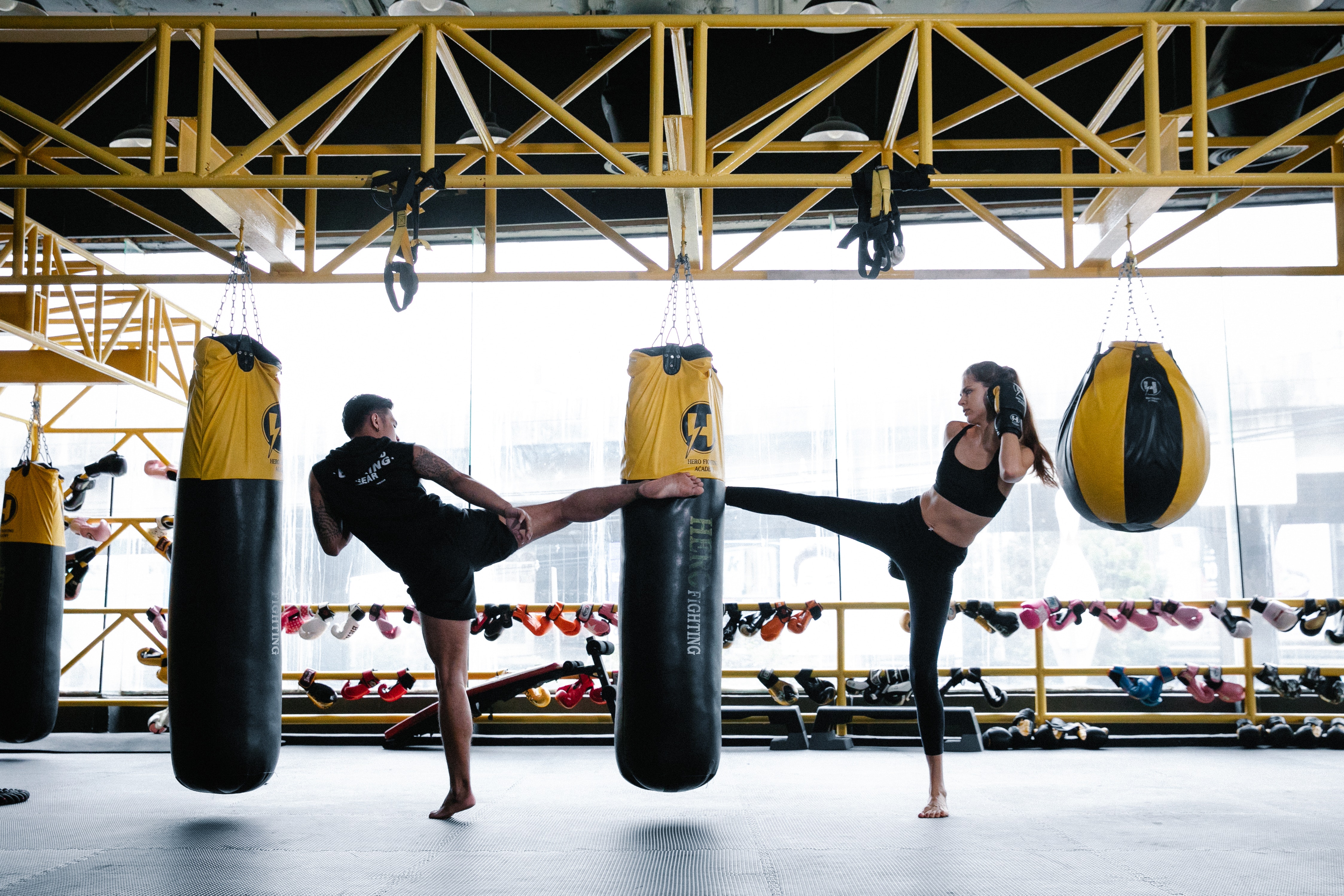 Woman and man both kicking a hanging heavy back with boxing gloves on