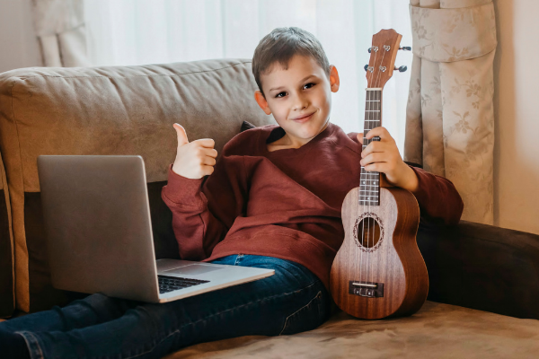 boy with ukulele and laptop on sofa