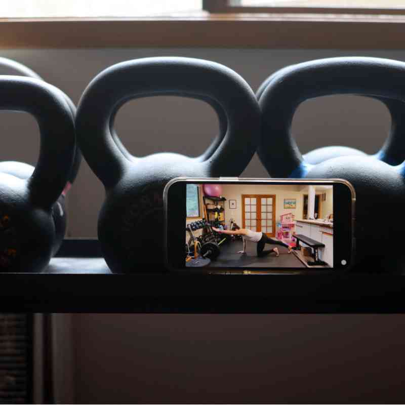 A photo of an exercise demo being played back on a phone, propped against a kettlebell rack.