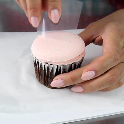 smoothing a cupcake top with acetate