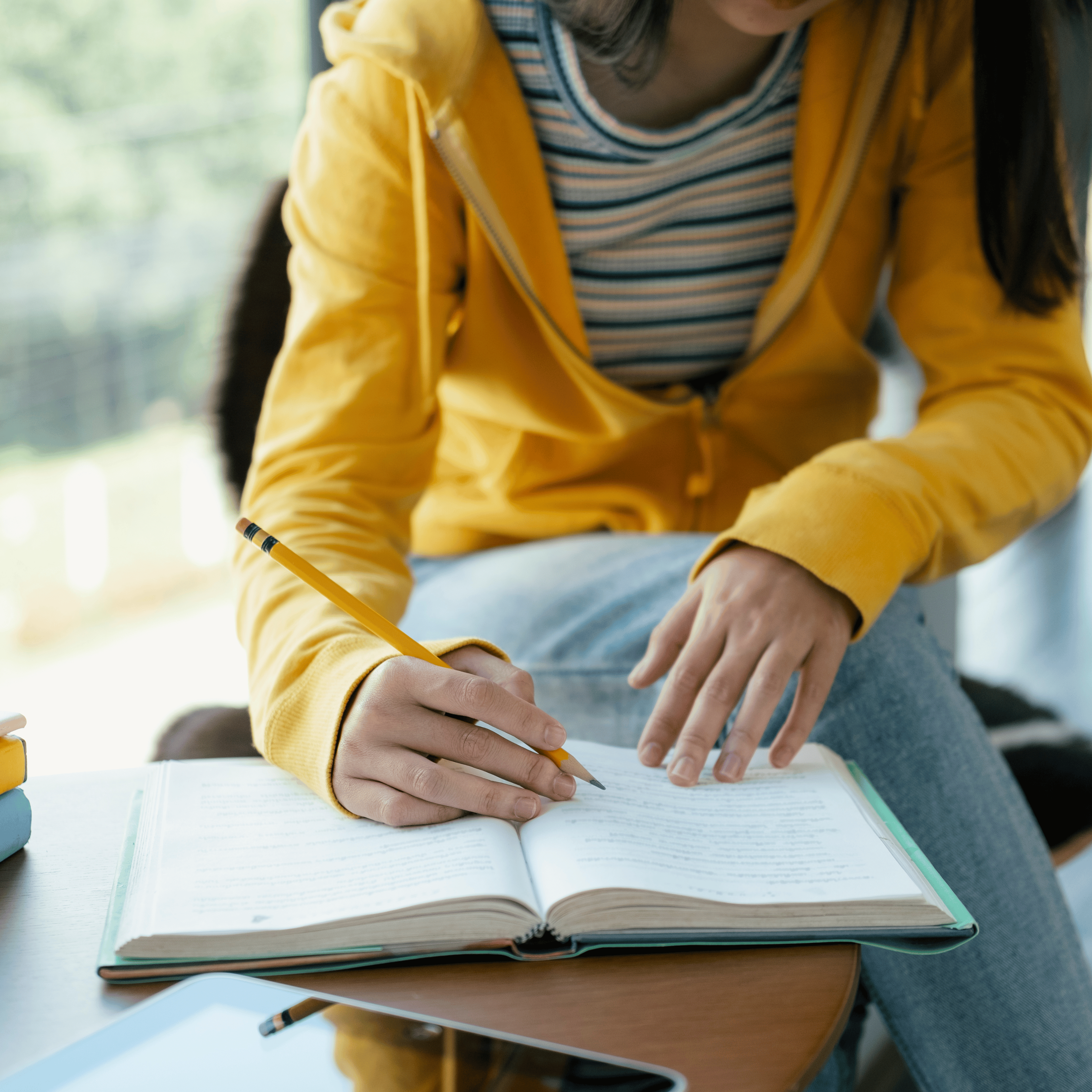 student wearing hoodie sitting at desk writing in a book