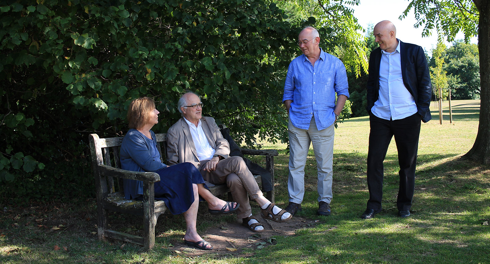 Teachers Christina Feldman and Stephen Batchelor seated on a bench outdoors in conversation with John Peacock and Akincano Weber standing beside them.